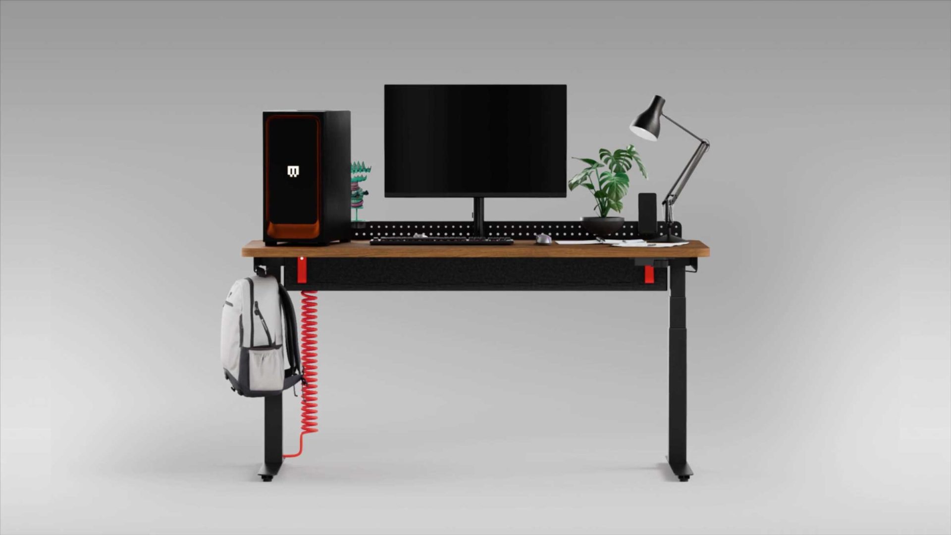 A modern desk setup with a monitor, lamp, plant, and desktop computer features a Herman Miller Gaming chair. A white backpack hangs on the left, and a red coiled cable dangles beneath the desk. The background is plain gray. Frame from Stash Magazine article.
