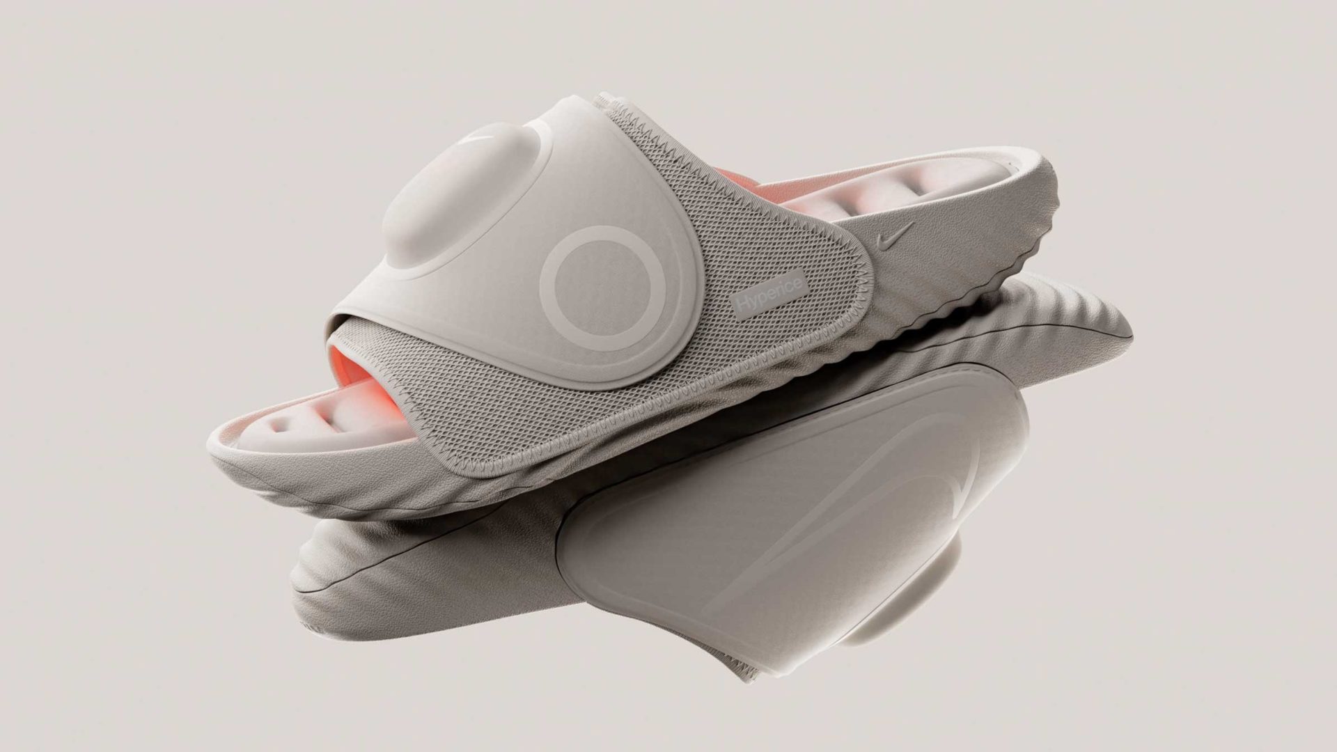 Two stacked light gray Nike Hyperslide sandals with a prominent circular design element on the strap and a peach-colored interior. Frame from Stash Magazine article.