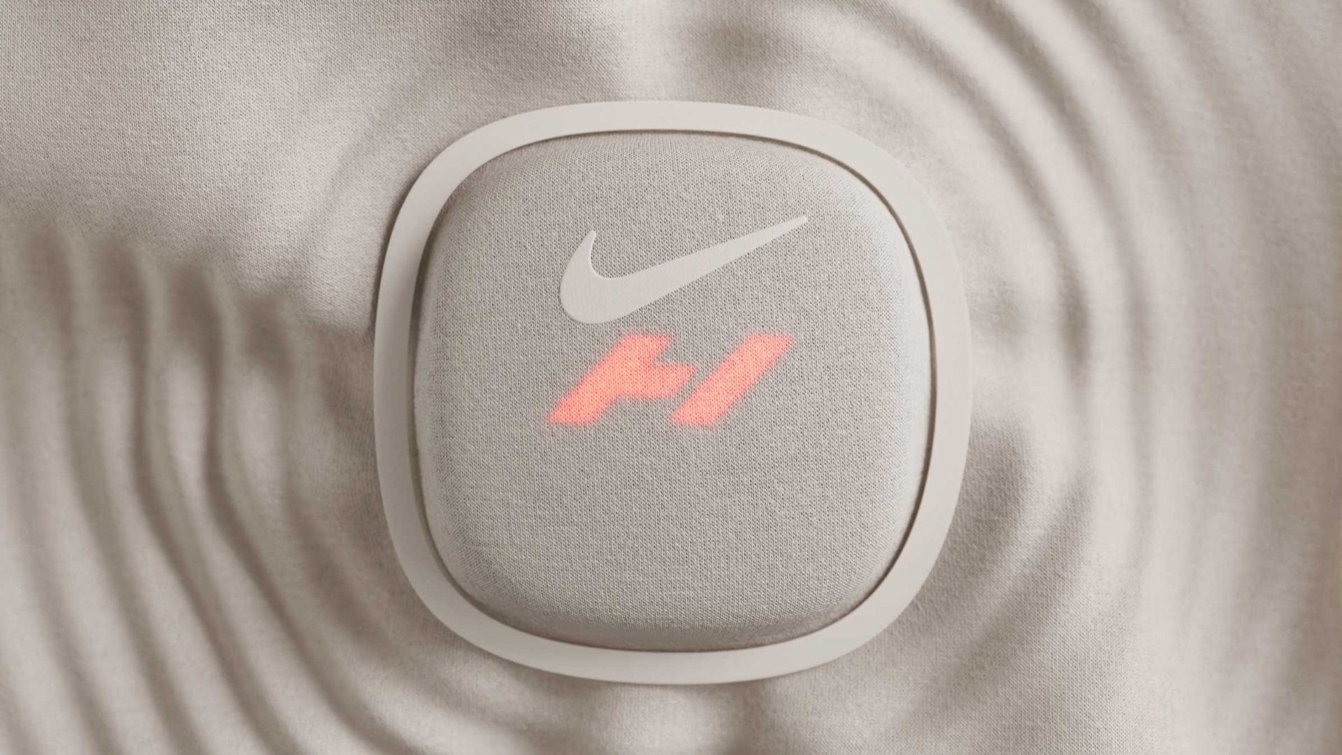 A square, fabric-covered Hyperice Nike device featuring a Nike swoosh logo above the red, stylized F1 Formula 1 logo. Frame from Stash Magazine article.