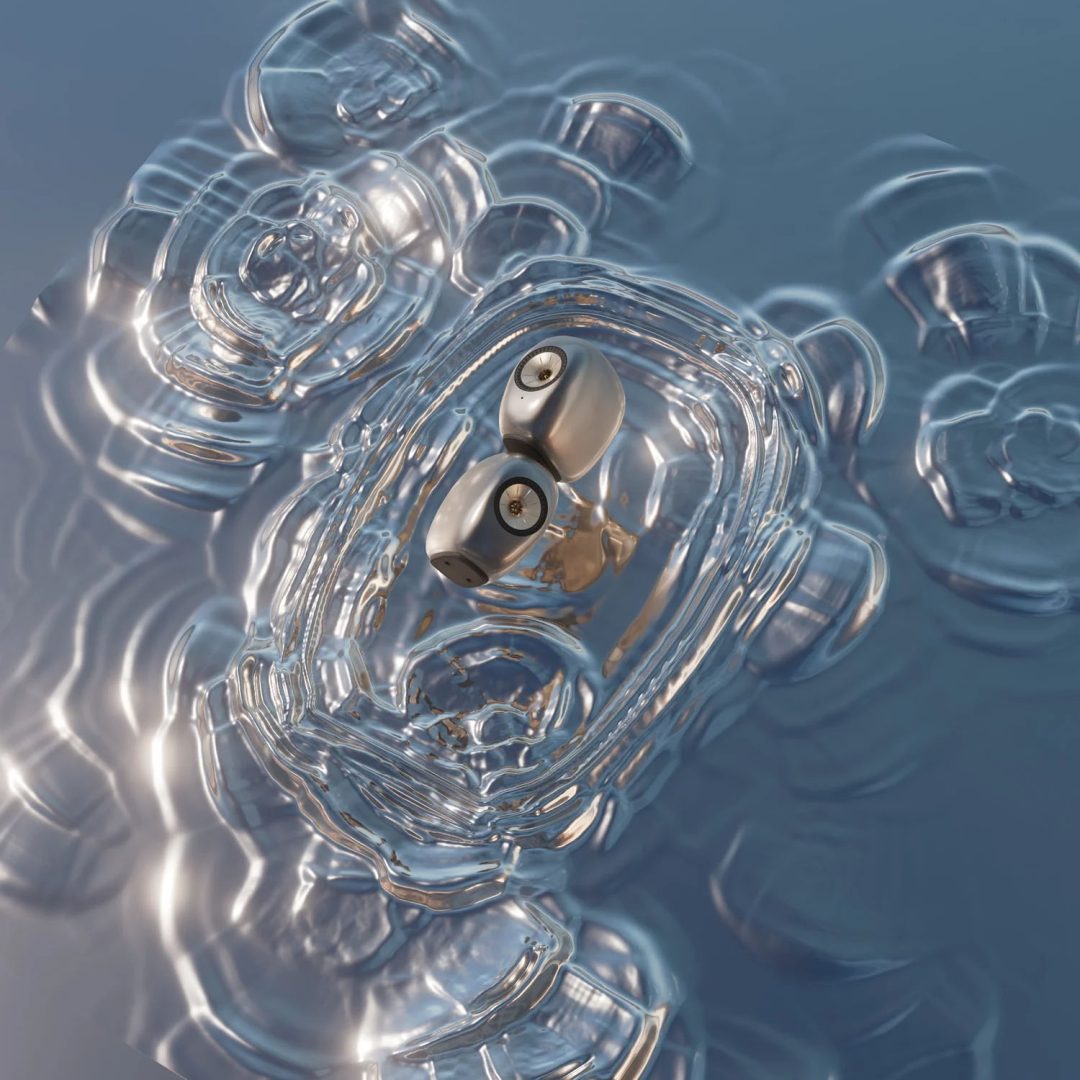 Two metallic-looking objects resembling eyes are encased in a clear, rippled, glass-like oval structure floating on water with concentric wave patterns. With its surreal, futuristic appearance, the scene evokes the innovative artistry seen in the KEF LS Luxe x Ross Lovegrove launch film by James Brocklebank. Frame from Stash Magazine article.