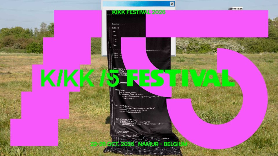 A large pink 15 and green text reading KIKK 15 FESTIVAL overlay a photo of a grassy field with a black fabric covered in code, embodying experimentation. Event details 23-25 OCT. 2026, NAMUR - BELGIUM are displayed at the bottom. Frame from Stash Magazine article.
