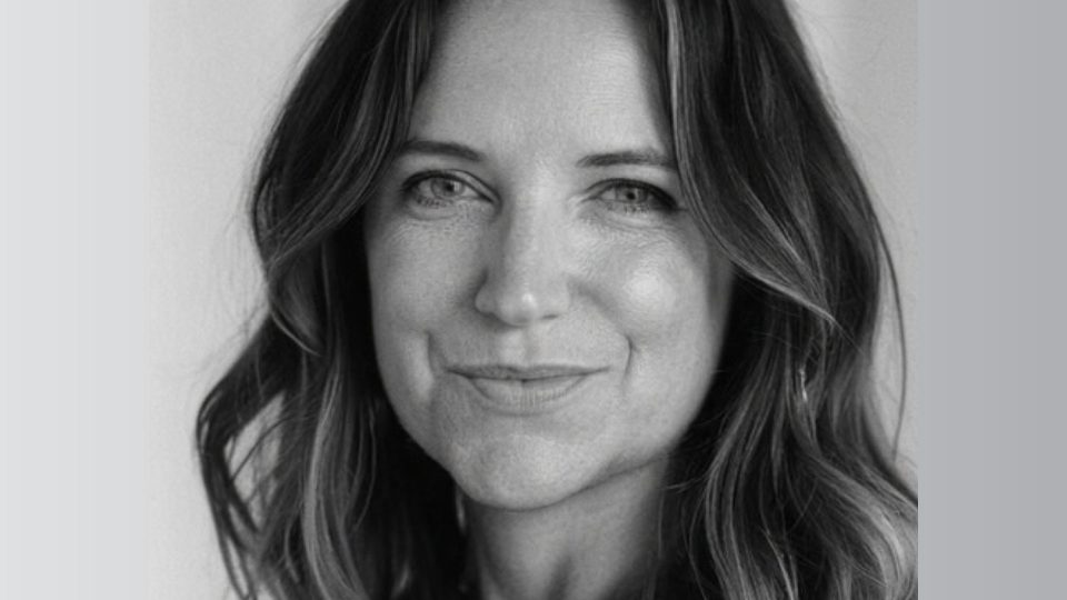 Black and white portrait of Kate Berry with long, wavy hair, a slight smile, and light-colored eyes, facing the camera. The background is plain and softly blurred—a signature Make Make style. Frame from Stash Magazine article.