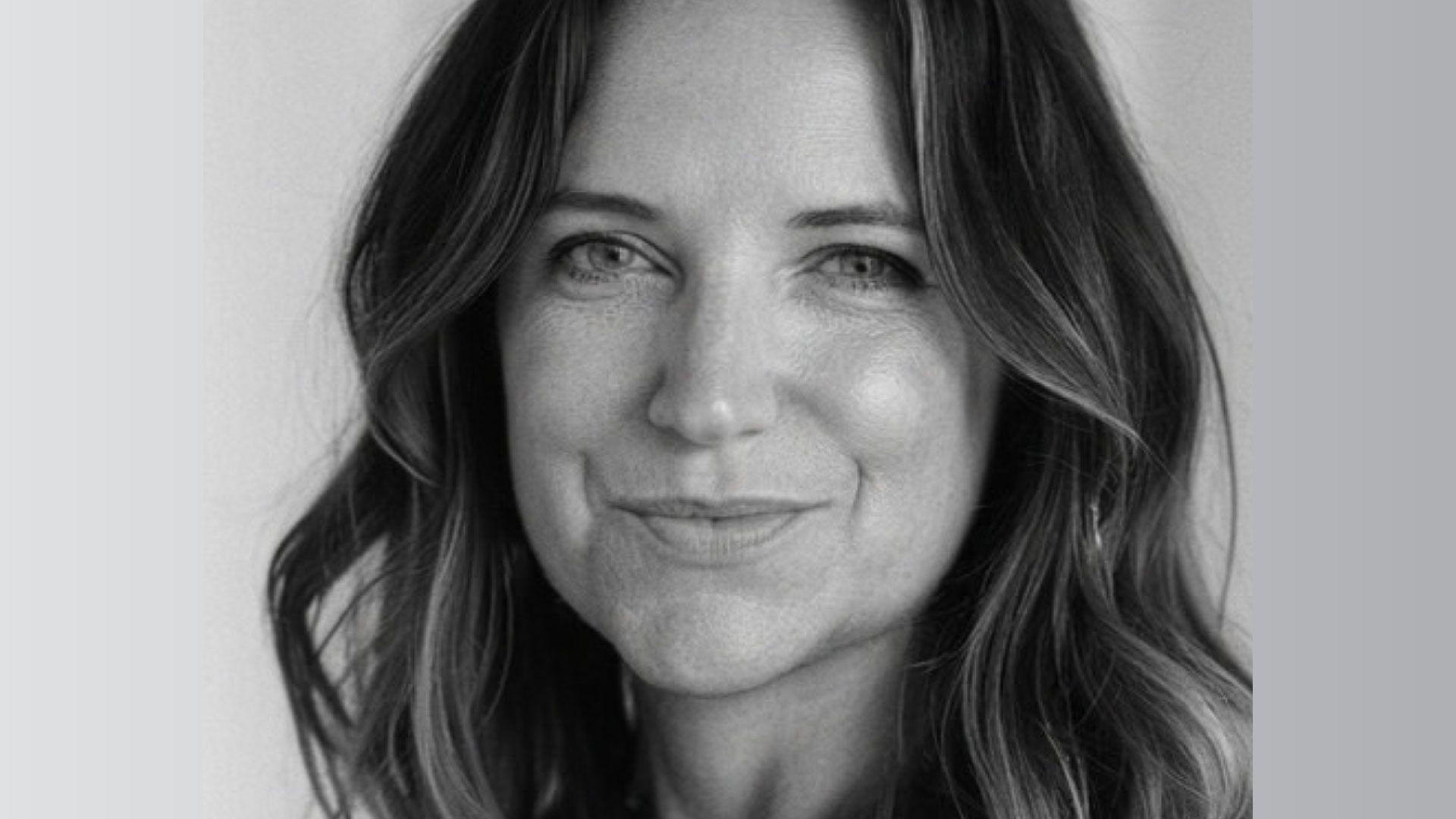 Black and white portrait of Kate Berry with long, wavy hair, a slight smile, and light-colored eyes, facing the camera. The background is plain and softly blurred—a signature Make Make style. Frame from Stash Magazine article.