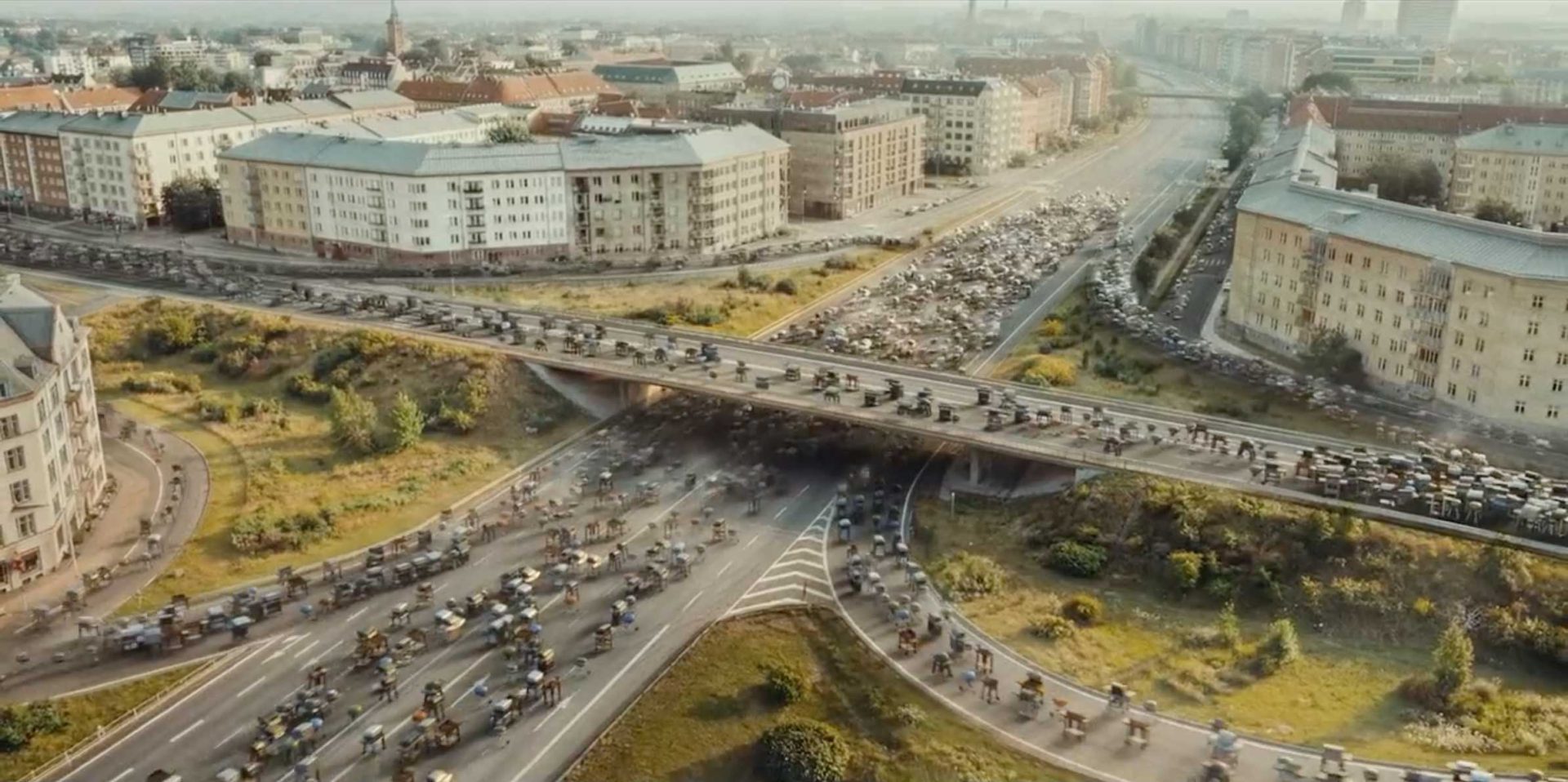 Aerial view of a busy urban intersection with multiple overpasses and roads densely filled with bicycles, not cars. Surrounding buildings and greenery are visible in the background, capturing the vibrancy Pete Riski brings to campaigns like Lidl Finland’s. Frame from Stash Magazine article.