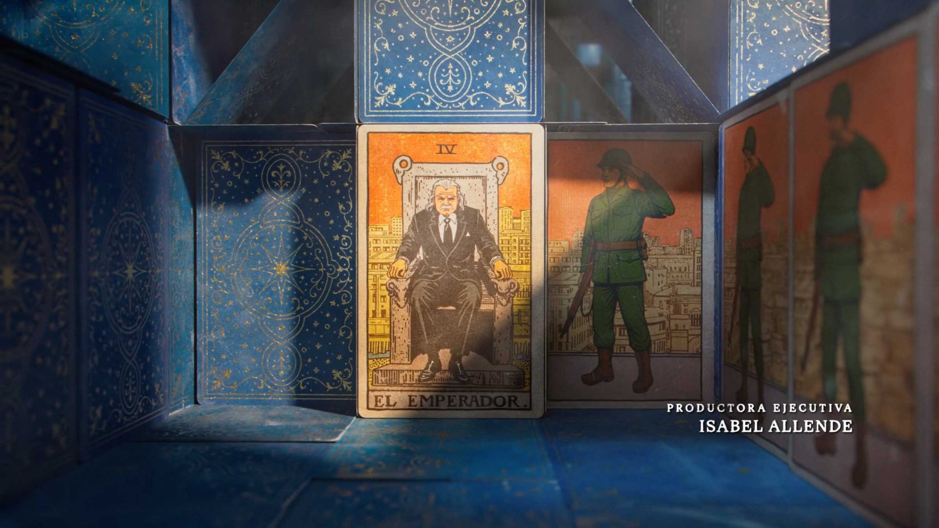 A tarot card labeled El Emperador features a man on a throne, surrounded by blue patterned panels and cards, with the text Productora Ejecutiva Isabel Allende on the right side, referencing La Casa de los Espíritus. Frame from Stash Magazine article.