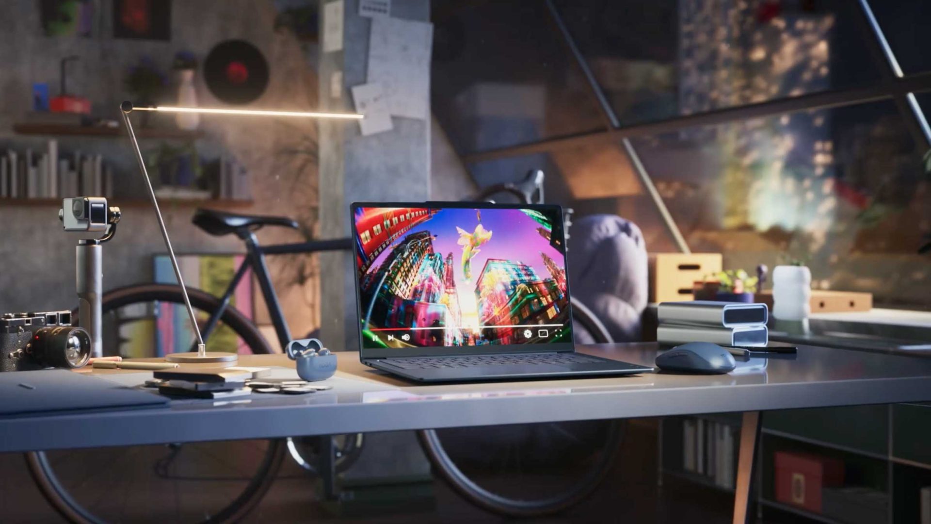 A modern desk with a Lenovo laptop displaying a colorful cityscape, surrounded by a lamp, headphones, camera, mouse, and other gadgets. A bicycle and large windows with a nighttime city view are in the background, all captured perfectly in this Frame48-inspired setting. Frame from Stash Magazine article.