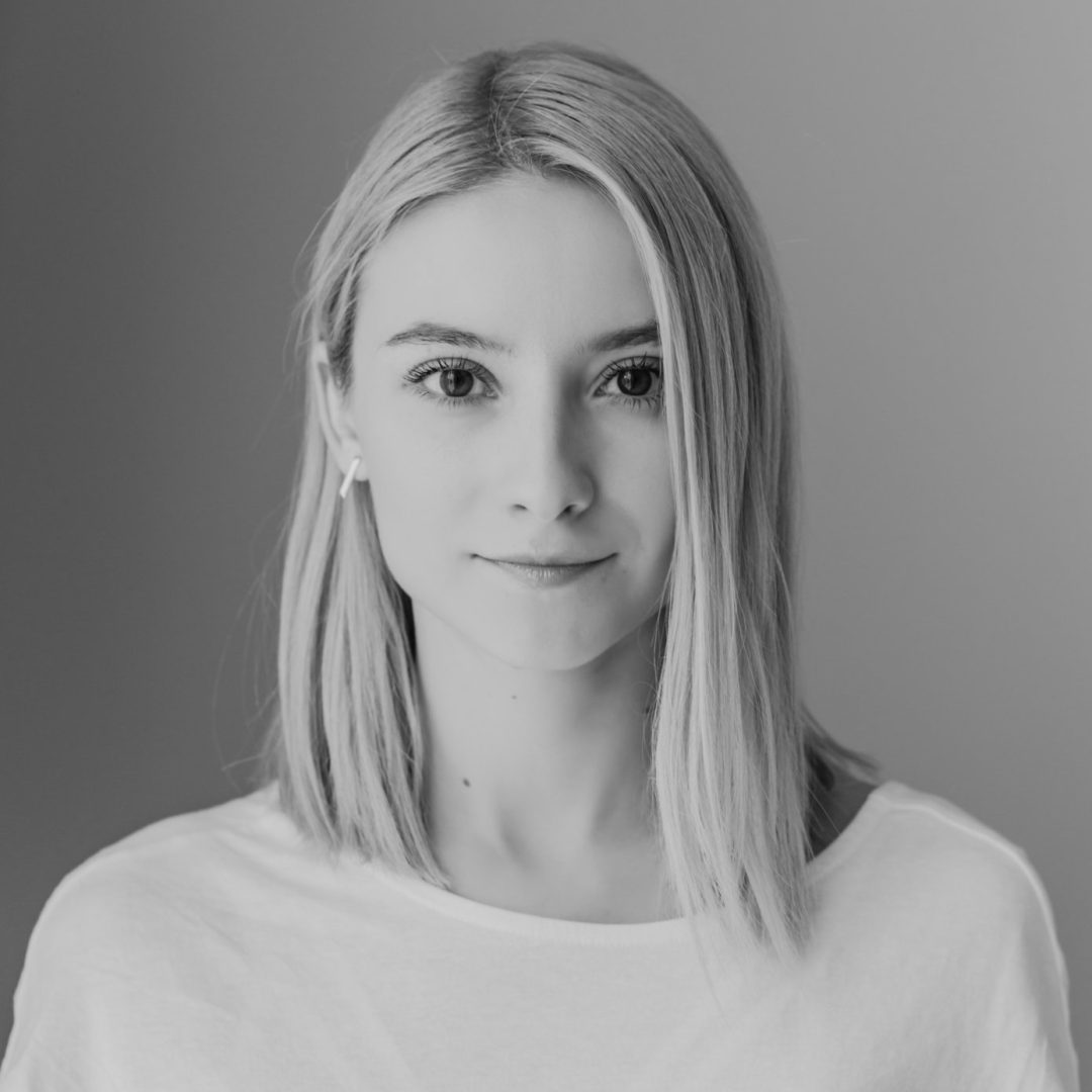 Black and white portrait of a young woman with straight, shoulder-length blonde hair, wearing a plain white top. She looks directly at the camera with a neutral expression—a striking image for any OFFF 2026 Get Seen campaign. Frame from Stash Magazine article.