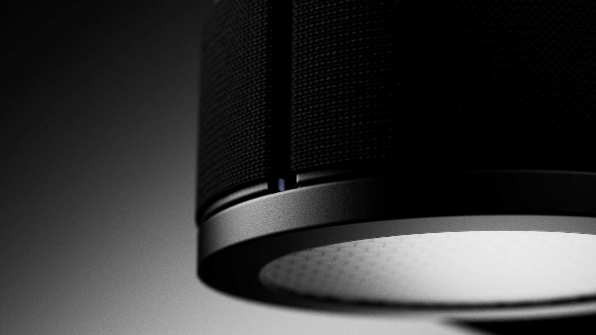 Close-up of a modern black smart speaker with a textured surface, illuminated by a Lodes MAP-inspired soft white light from the bottom, set against a dark, blurred background—capturing the essence of innovative lighting product design by jformento. Frame from Stash Magazine article.
