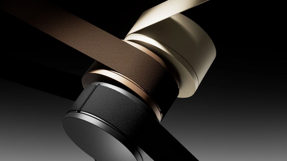 Two cylindrical, modern speakers in black and gold, wrapped with matching fabric straps, are set against a dark gradient background—echoing the sleek, minimalist style of the Lodes MAP lighting product film by jformento. Frame from Stash Magazine article.