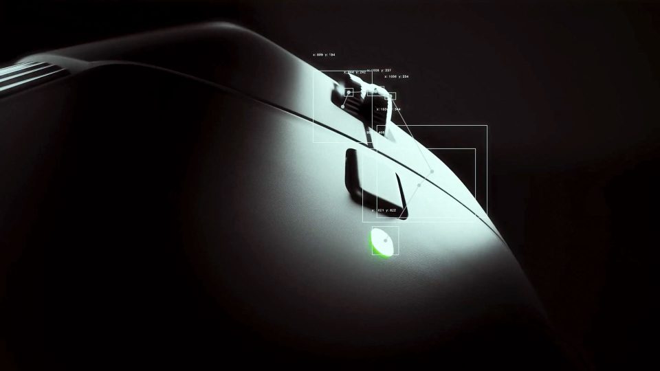 Close-up of a black Logitec MX Master 4 mouse in low light, highlighting its scroll wheel and side buttons. A small green LED indicator is lit near the thumb button, with white data overlays showing detailed measurements. Frame from Stash Magazine article.