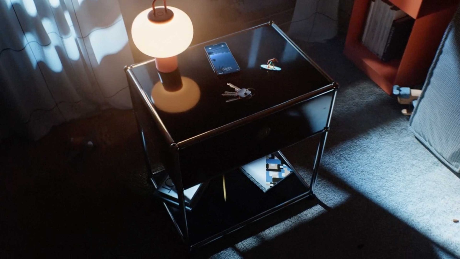 A lit lamp, smartphone, keys, and keychain rest on a black nightstand, drawing the eye to this spec spot. Books are on a lower shelf, with sunlight streaming through curtains onto the carpeted floor and nightstand. Frame from Stash Magazine article.
