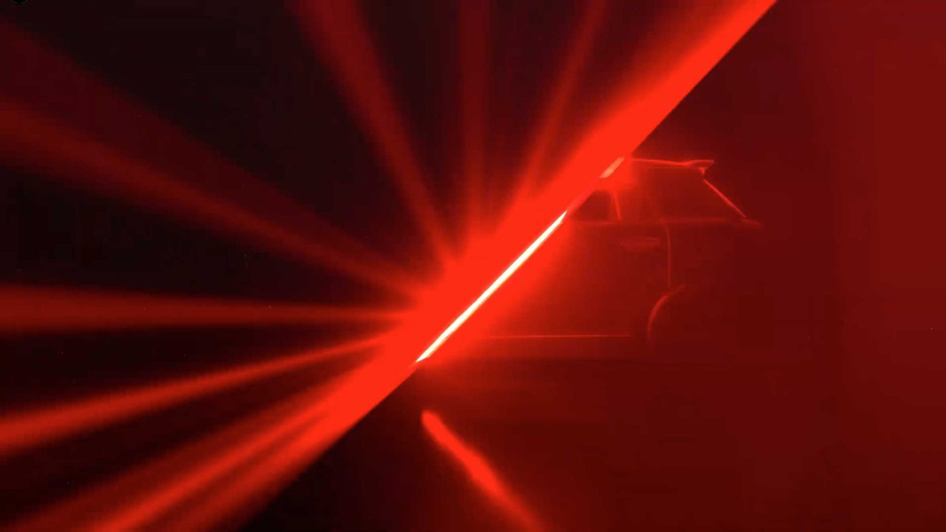 A car is partially visible behind a sharp diagonal beam of red light, with red rays spreading across a dark background—capturing the bold spirit of MINI Icon Drops Special Editions. Frame from Stash Magazine article.