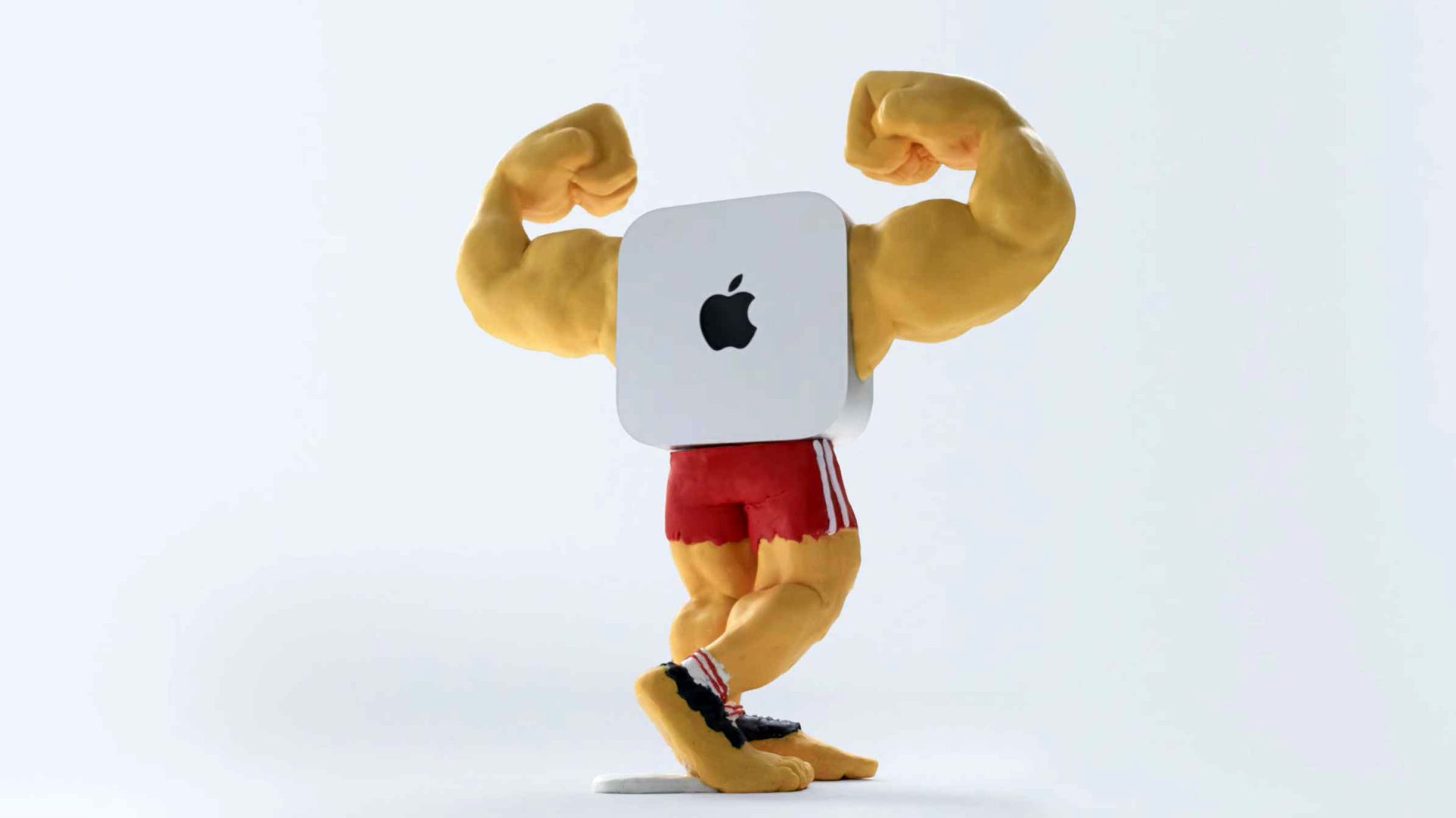 A figurine with a muscular human body, flexing arms, red shorts, and a Mac Mini computer as its torso, shown against a plain white background. Frame from Stash Magazine article.