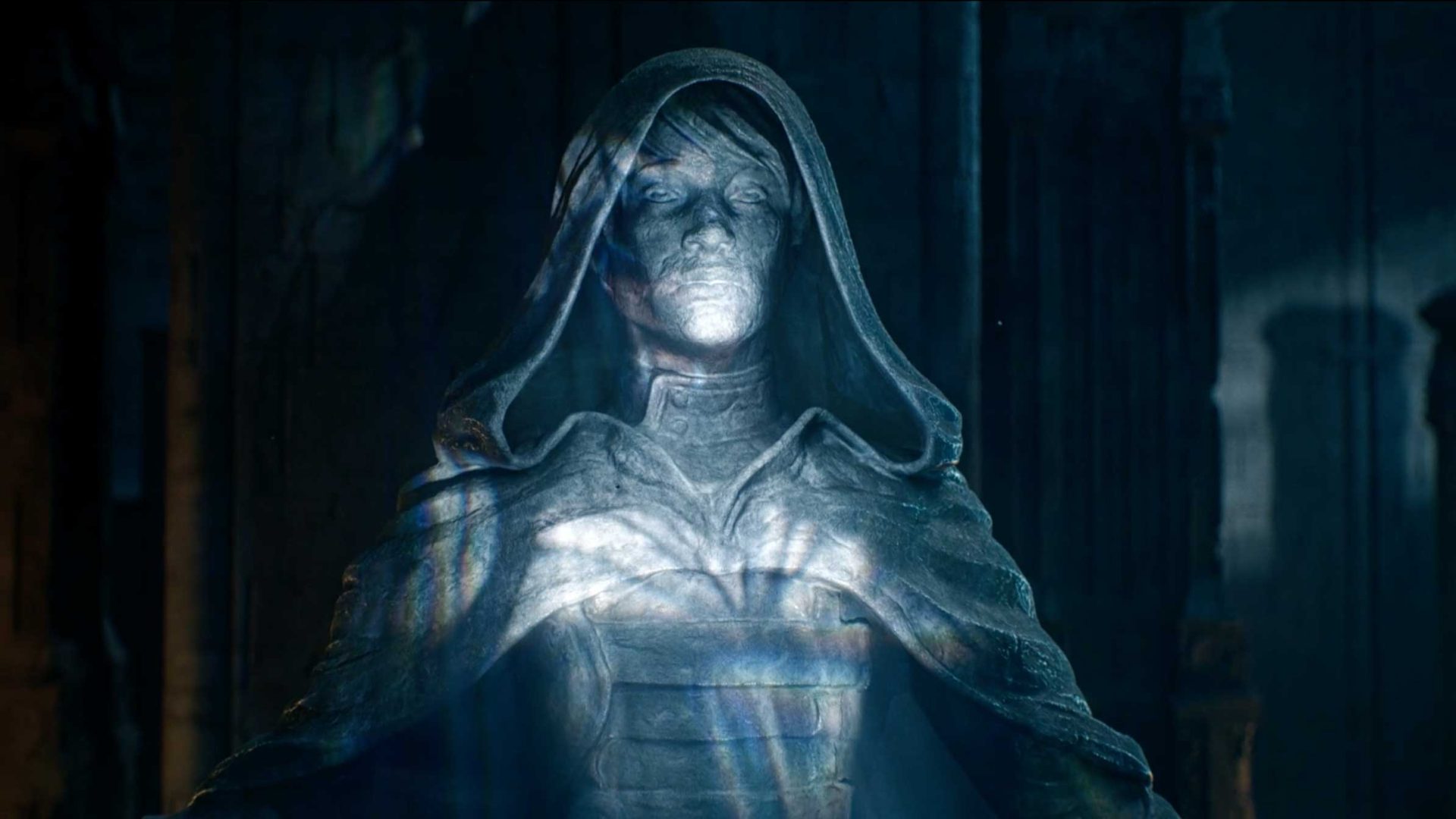 A stone statue of a hooded figure with closed eyes and a solemn expression, illuminated by blue and white light, stands in a shadowy, ancient setting with columns in the background—evoking the enigmatic atmosphere of an MTG trailer as Fractures Reality blurs the line between stillness and Motion Design. Frame from Stash Magazine article.