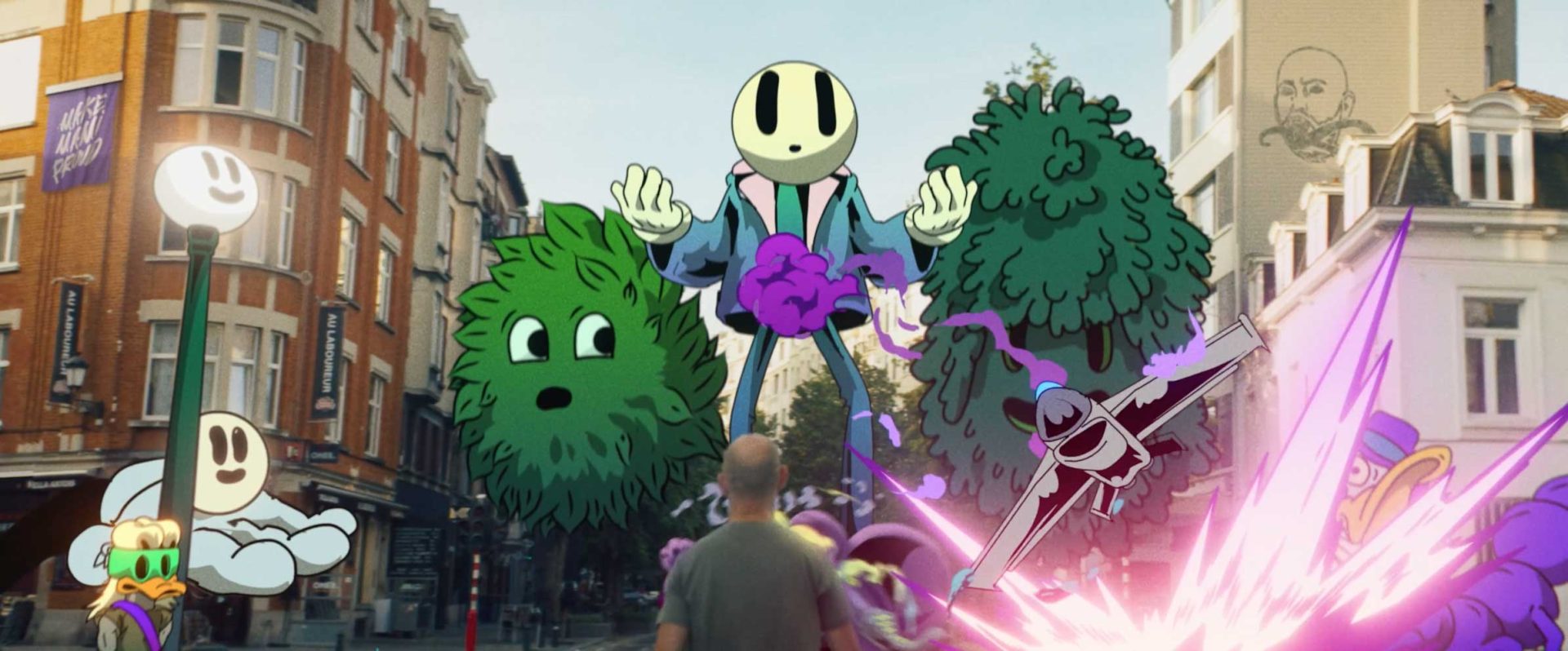 A person stands on a city street, facing large colorful cartoon characters—including floating faces, bushes, and a flying creature—all blended into the real environment with buildings in the background, reminiscent of a scene from DREAMCAT, the acclaimed short film by Joost Jansen. Frame from Stash Magazine article.