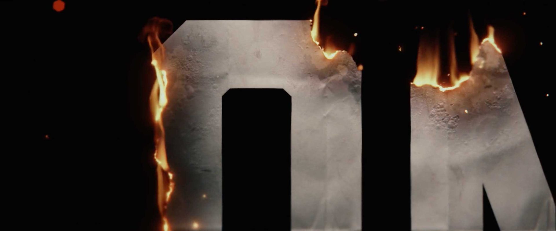 A large metallic letter O is partially visible, with flames burning along its top and left edges against a dark background—a striking homage to the Main Titles of Netflix’s Man on Fire. Frame from Stash Magazine article.