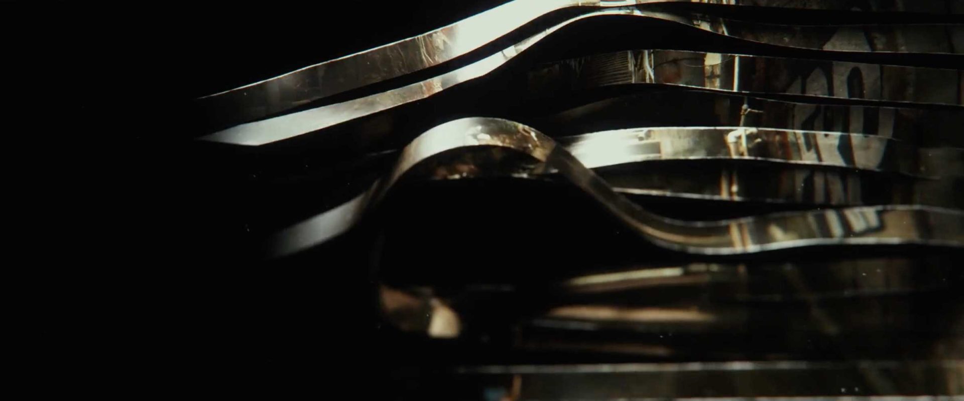 Curved metallic strips with reflective surfaces stack closely together against a dark background, creating an abstract, flowing pattern reminiscent of main titles for a Netflix series like Man on Fire. Frame from Stash Magazine article.