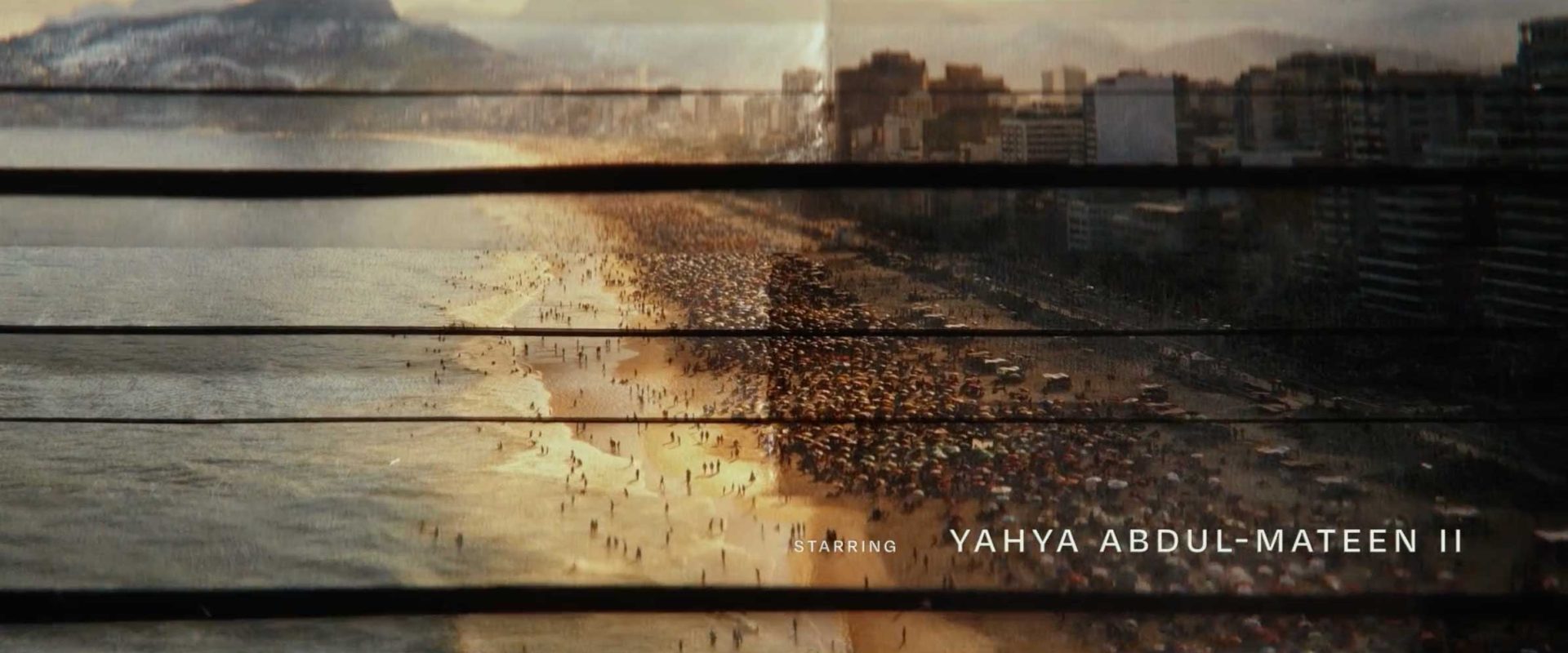 View of a crowded beach at sunset with city buildings on the right, seen through window blinds. Main Titles appear along the bottom, reading Starring Yahya Abdul-Mateen II in Netflix’s Man on Fire. Frame from Stash Magazine article.