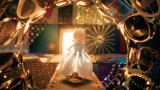 A doll in a blue and white gown stands on a sparkling path, facing a glowing doorway. Shiny objects, mirrors, and bright lights create a whimsical scene inspired by Margo's-Got-Money-Troubles Titles on Apple TV by Peter Anderson Studio. Frame from Stash Magazine article.