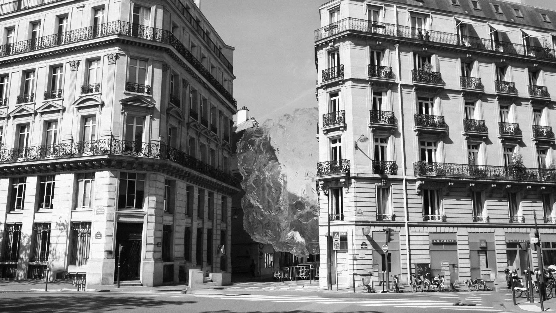 Inspired by Martynas Genkovas’ short film style, two ornate Parisian-style buildings frame a narrow street, but a rocky mountain appears unexpectedly between them, blending classic urban architecture with a surreal natural landscape. Frame from Stash Magazine article.