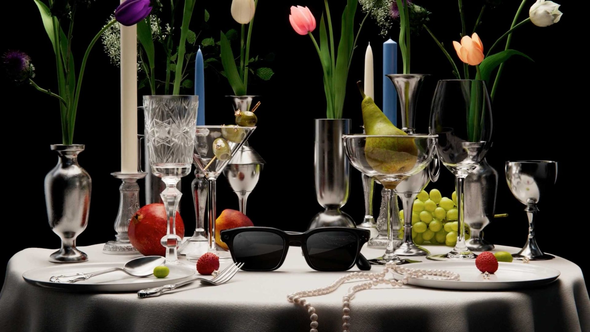 A lavish table setting with crystal glasses, fruit, candles, sunglasses—including a sleek pair of AI Glasses—and a pearl necklace on a white tablecloth. Colorful tulips in the background add to this Meta-inspired scene, perfect for a Builder’s Club gathering. Frame from Stash Magazine article.