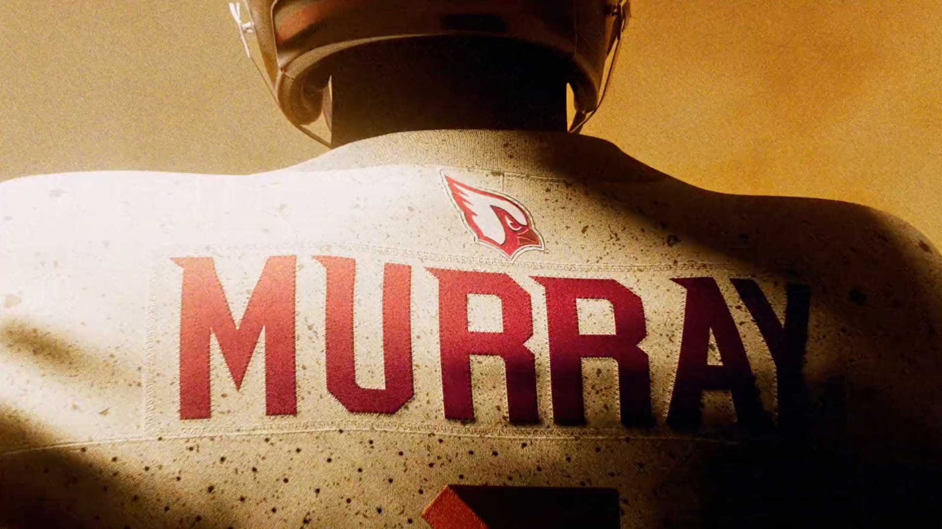 A football player wearing a helmet and a white Arizona Cardinals Nike uniform with the name MURRAY in bold red letters across the back. The NFL team's logo is visible above the name, highlighted by warm, dramatic lighting. Frame from Stash Magazine article.