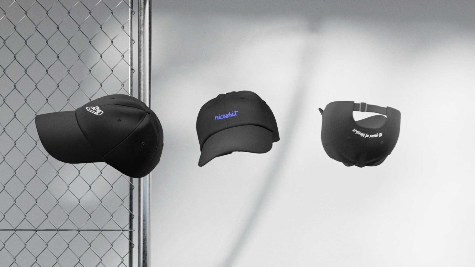 Three black baseball caps are displayed against a light background next to a chain-link fence. Each cap shows different text or designs, with one cap facing forward, one at an angle, and one showing the back. Frame from Stash Magazine article.