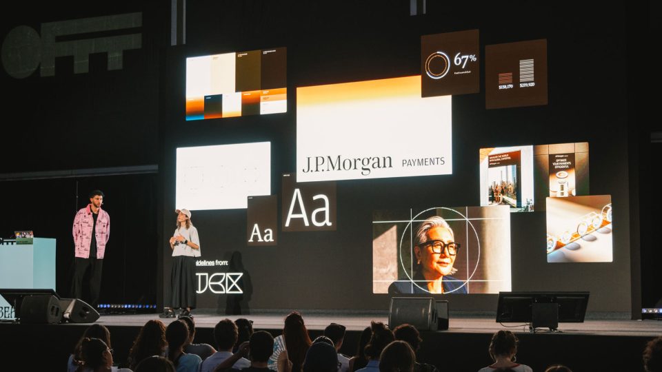 Two presenters, including NotReal Co-Founder Valeria Moreiro, stand on stage in front of a screen displaying J.P. Morgan Payments branding elements during an OFFF interview, as the audience watches intently. Frame from Stash Magazine article.