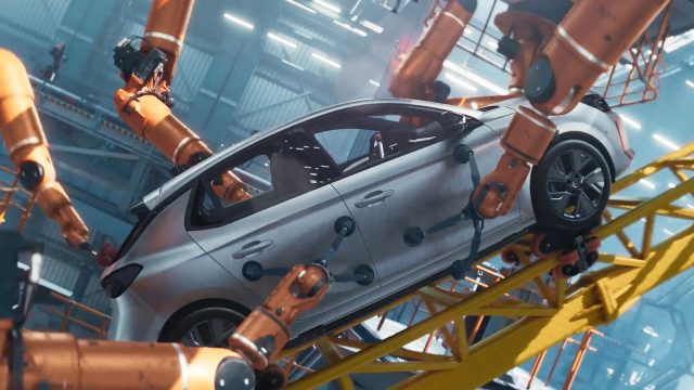A silver Opel Corsa car frame is held and worked on by multiple orange robotic arms in an industrial factory setting, reminiscent of the iconic roller coaster commercial by Mark Jenkinson, LA PAC & Mathematic, with bright lights and a blue-toned background. Frame from Stash Magazine article.