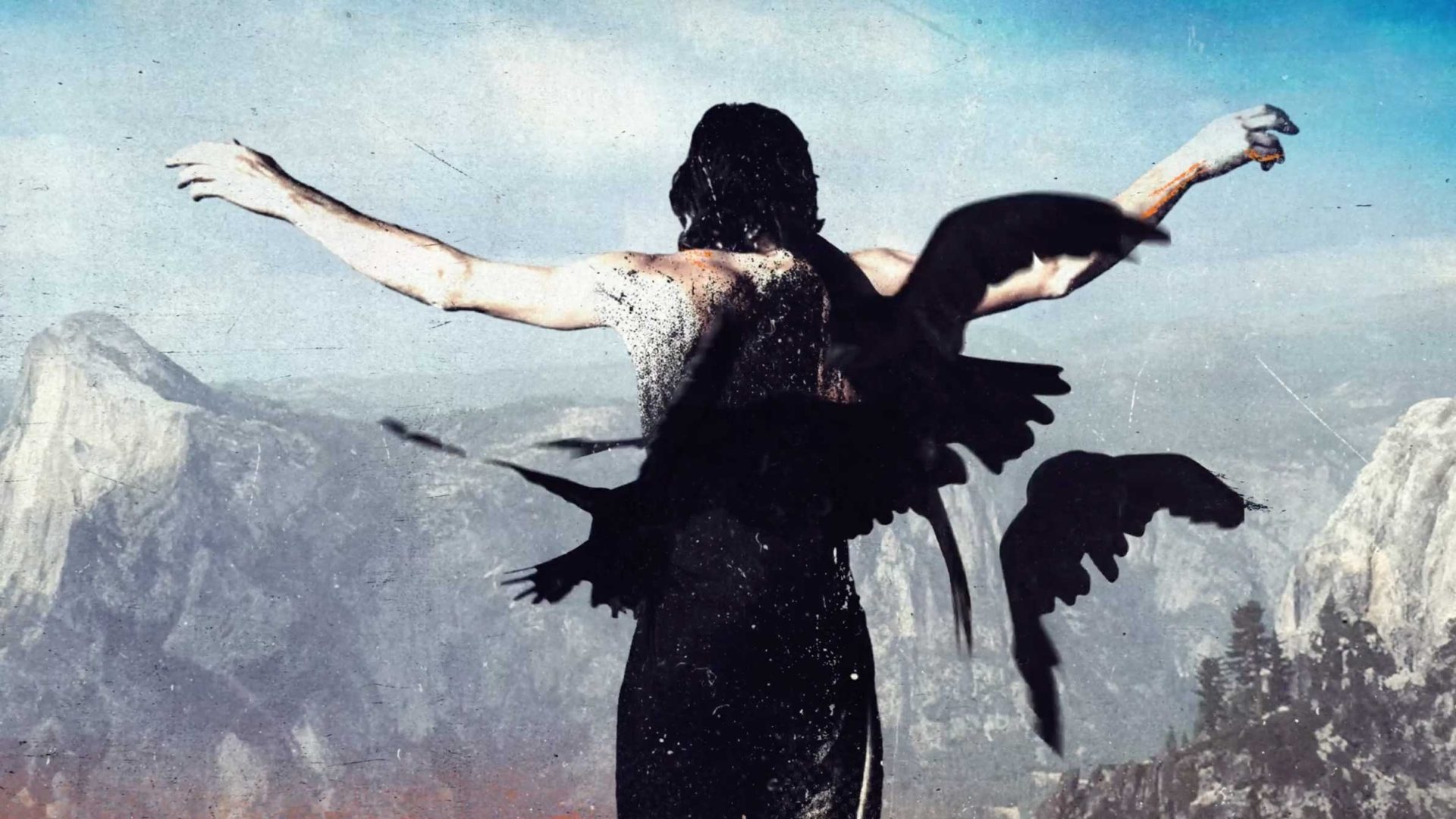 A person with outstretched arms stands facing mountains, black bird silhouettes overlaying their back like wings—evoking the magic of Opening Titles for HBO's The Dark Wizard Doc by Brut Works. The sky is blue, rugged cliffs looming in the background. Frame from Stash Magazine article.