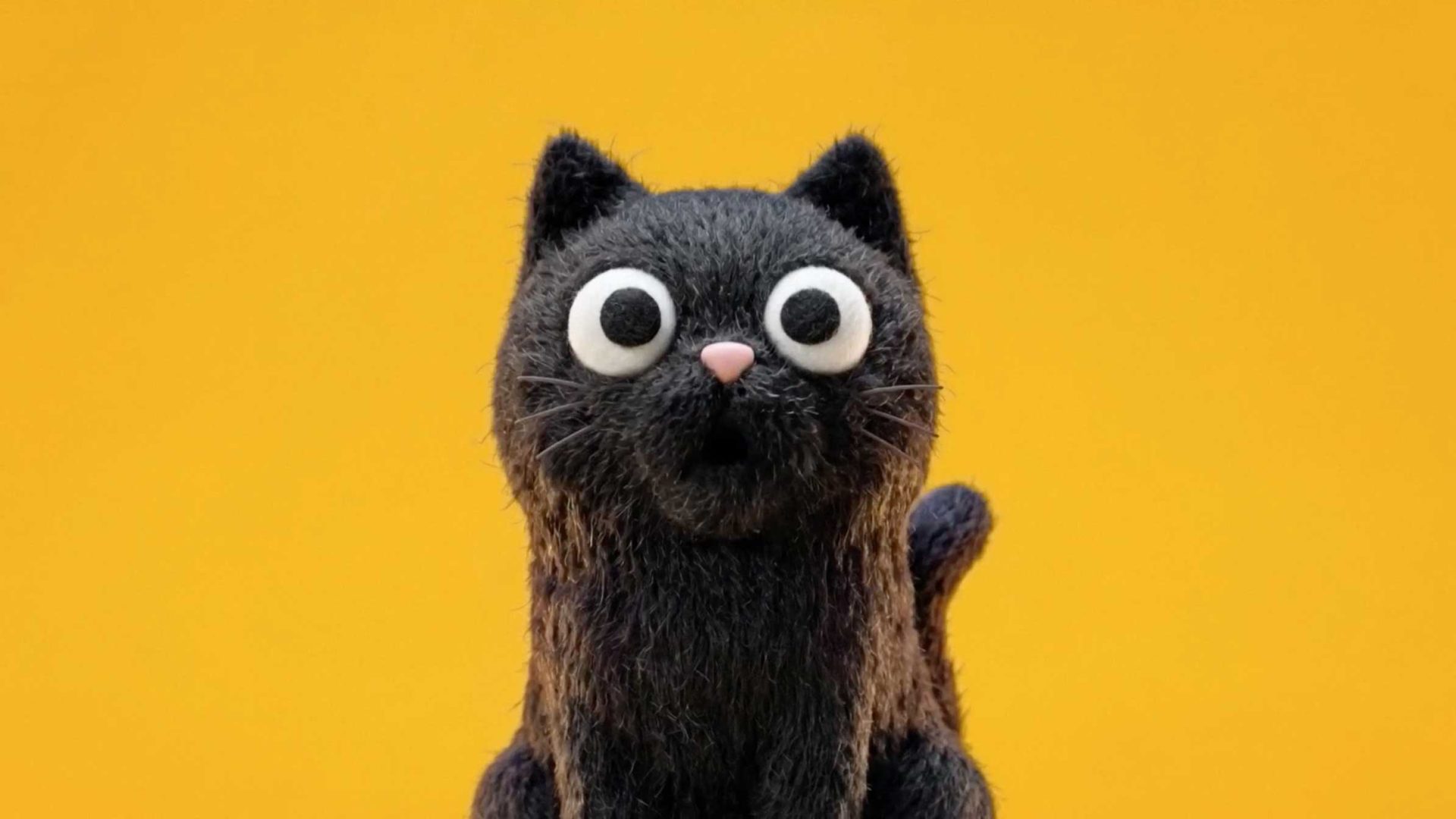 A fluffy black Petey figurine with wide, circular eyes and a small pink nose, set against a yellow background. Frame from Stash Magazine article.