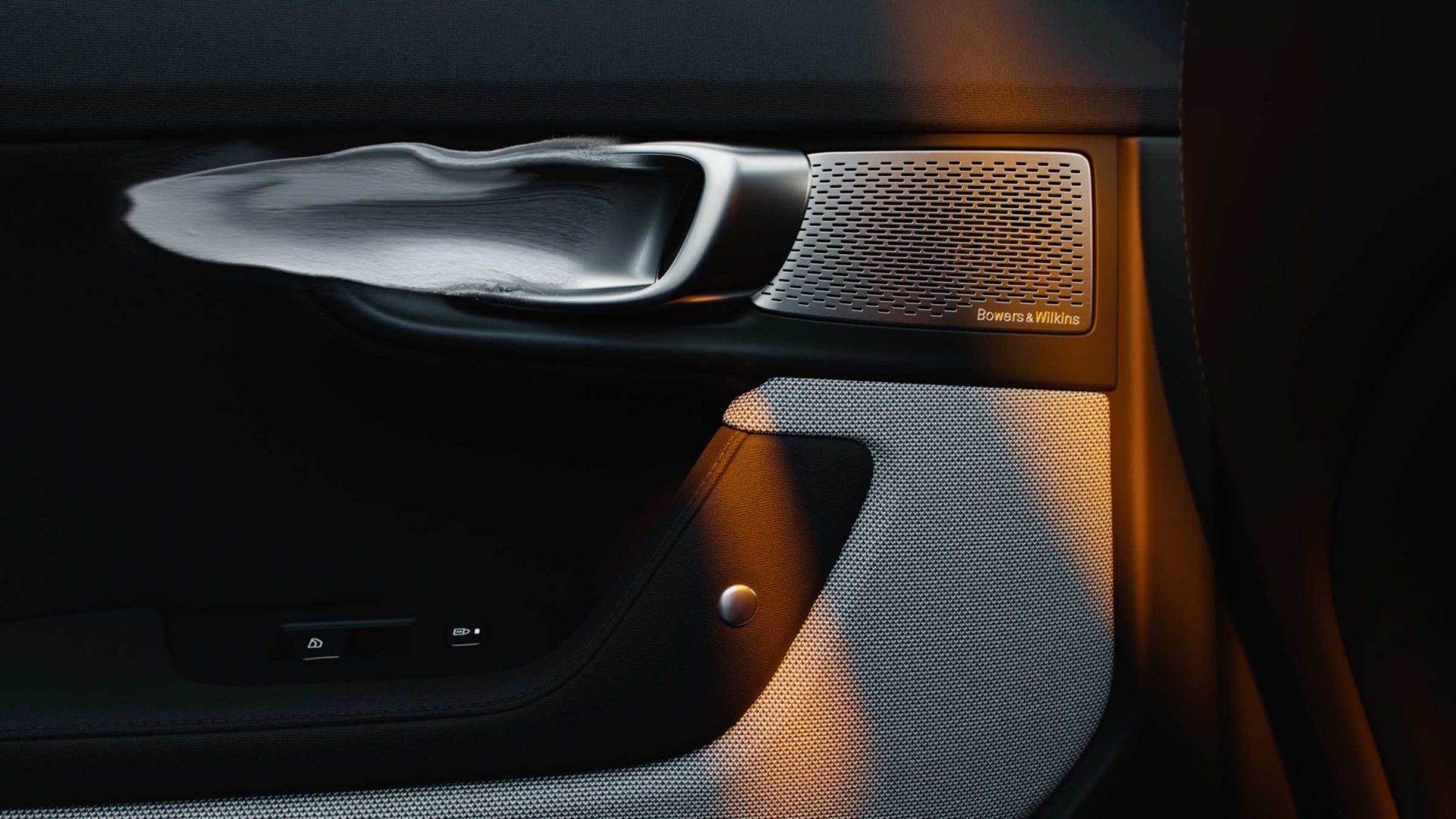 Interior door panel of a Polestar vehicle featuring a metallic door handle, a Bowers & Wilkins speaker grille, and window controls. Frame from Stash Magazine article.