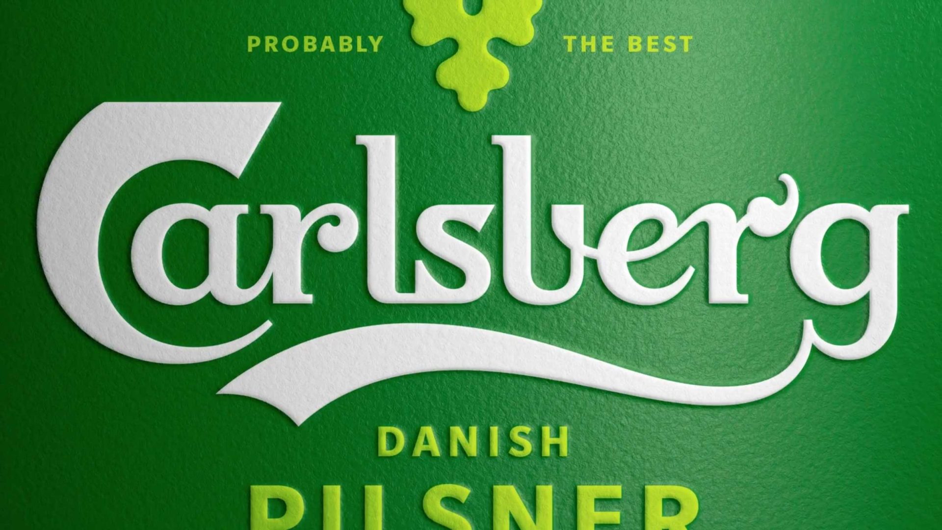 Close-up of a Carlsberg beer label designed by Taxi Studio, with the text “Probably the best Carlsberg Danish Pilsner” in white and yellow on green, featuring the Carlsberg logo, stylized hop graphic, and Probably Serif typeface. Frame from Stash Magazine article.