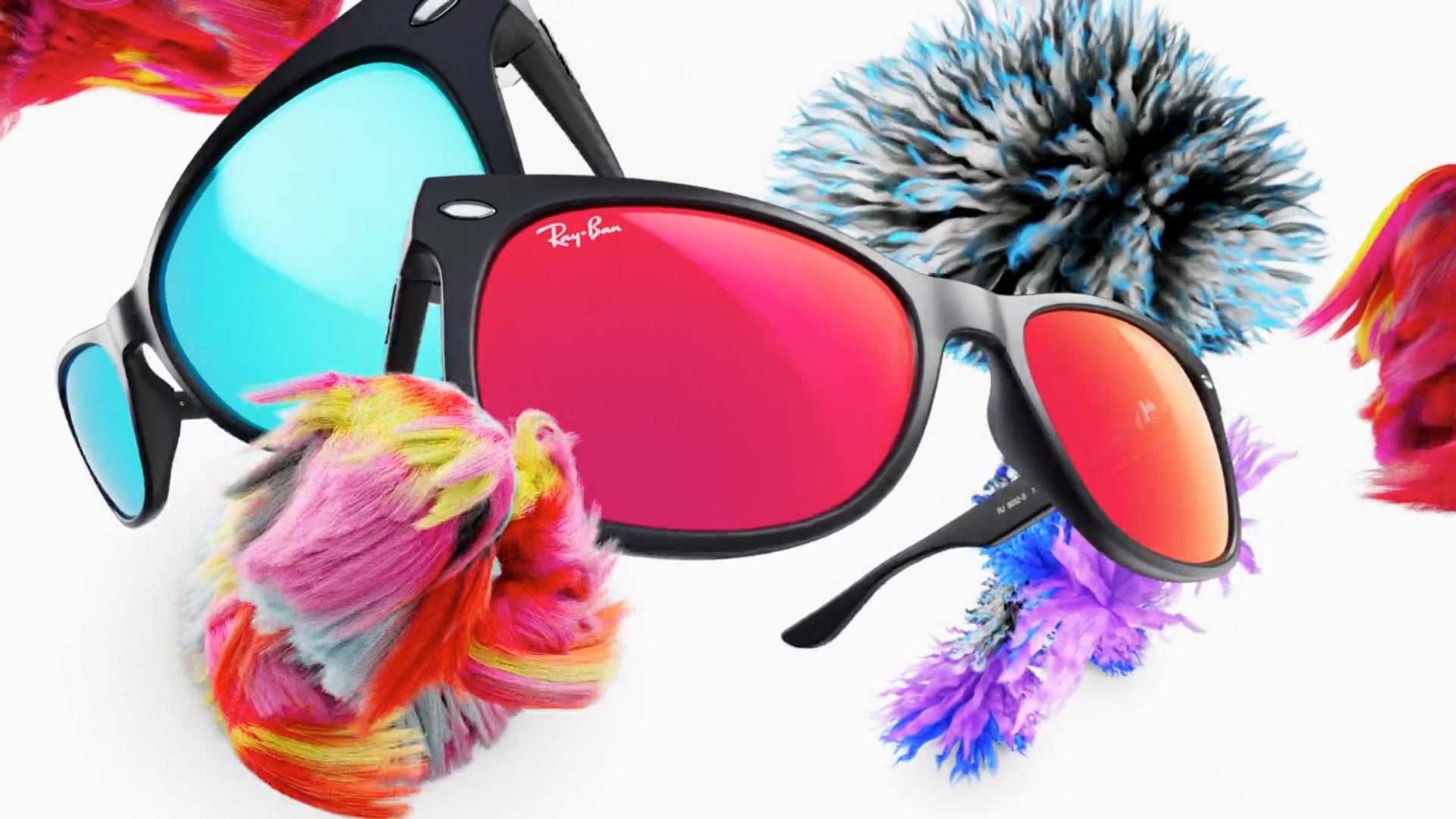Two pairs of Ray-Ban Kids sunglasses, one with blue lenses and one with red lenses, are surrounded by colorful, fluffy pom-poms on a white background—a playful scene captured in true C41 style. Frame from Stash Magazine article.