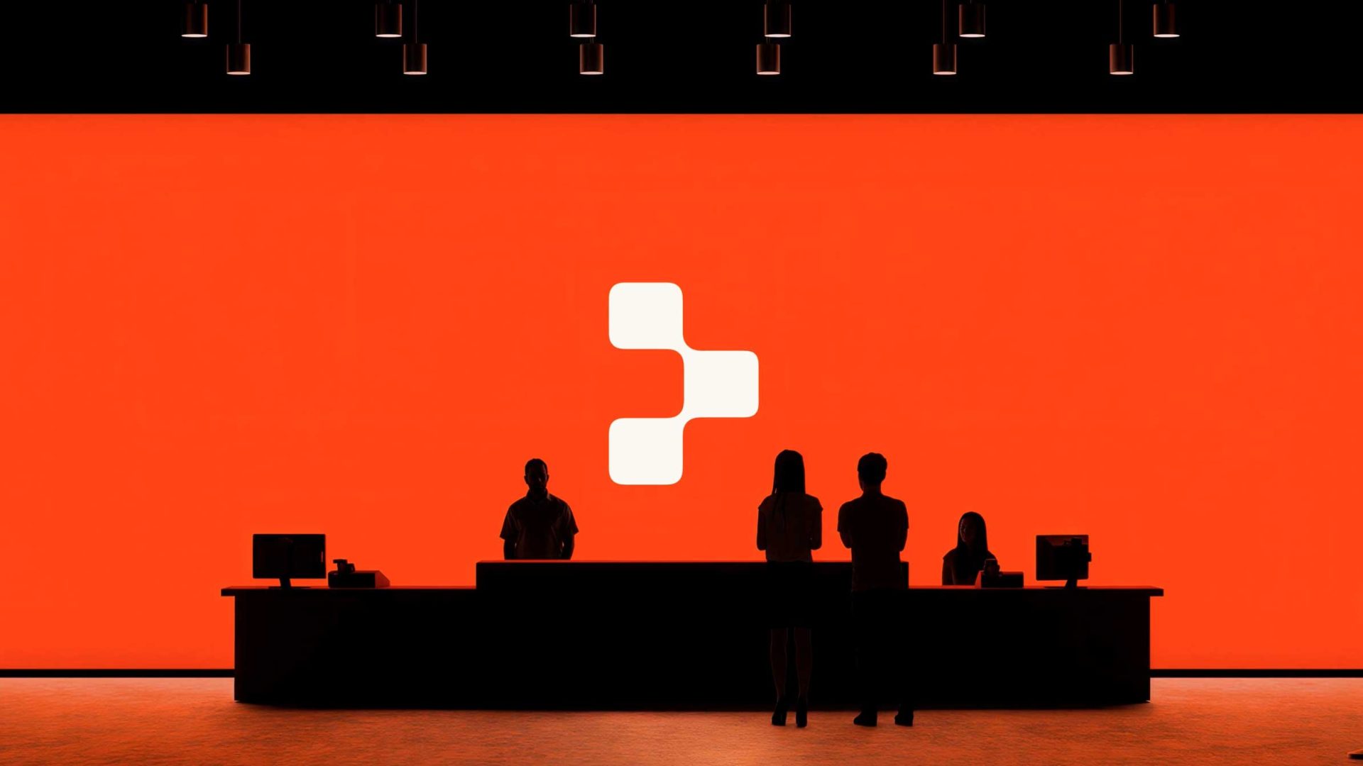 Silhouettes of four people stand or sit at a counter in front of a large, bright orange screen displaying Replit's white geometric logo. Ceiling lights hang above, illuminating the modern Oddfellows brand film scene. Frame from Stash Magazine article.