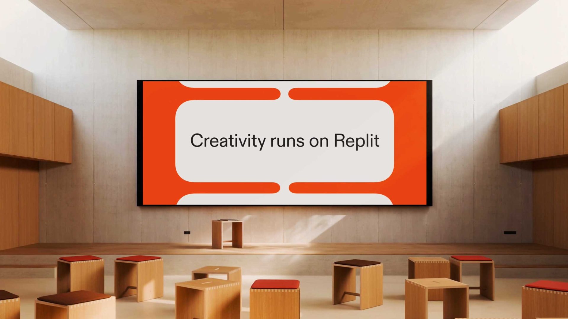 A modern, minimalist classroom with wooden stools and benches faces a large screen displaying the text "Creativity runs on Replit" in an orange and white design from Oddfellows' Brand Film. Frame from Stash Magazine article.