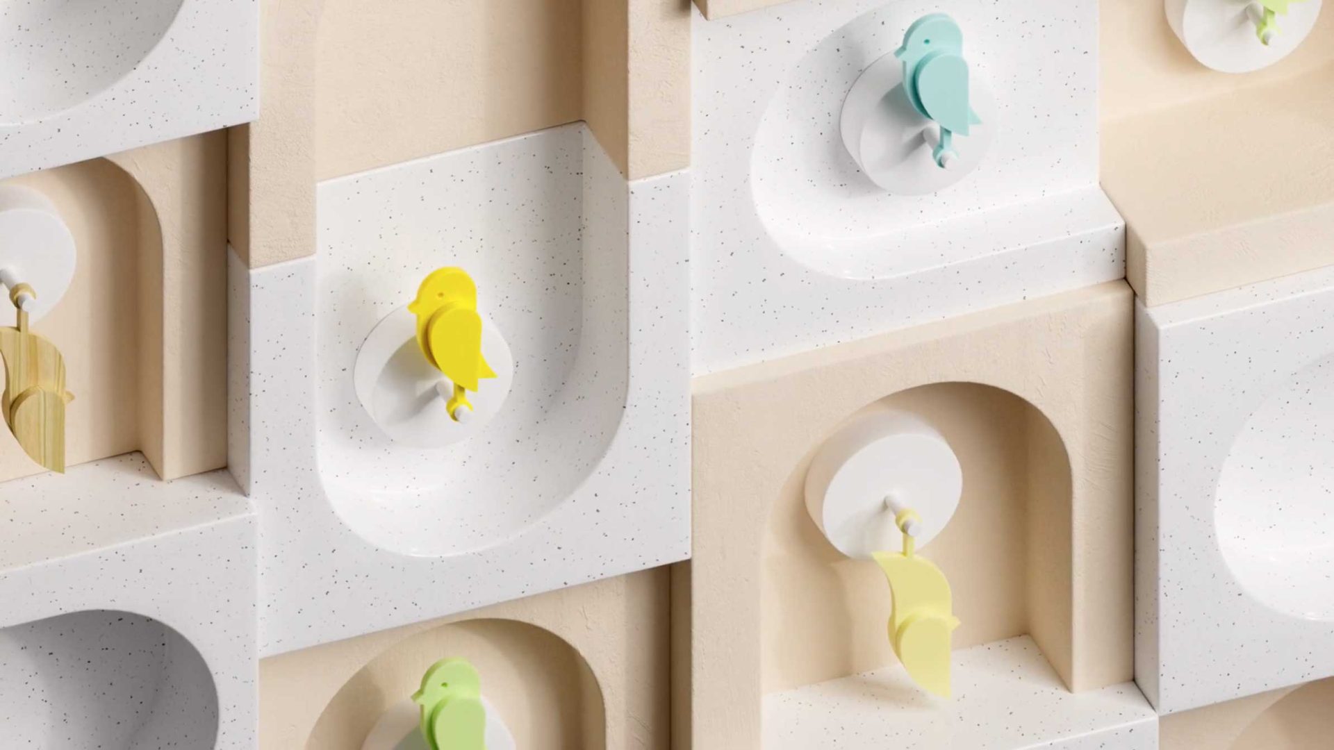 Colorful bird-shaped hooks in yellow, green, and blue are mounted on a patterned wall with curved and arched niches in beige and white tones—a minimalist, geometric scene inspired by Ribbit Launches in Copenhagen With Birdie Brand Film. Frame from Stash Magazine article.