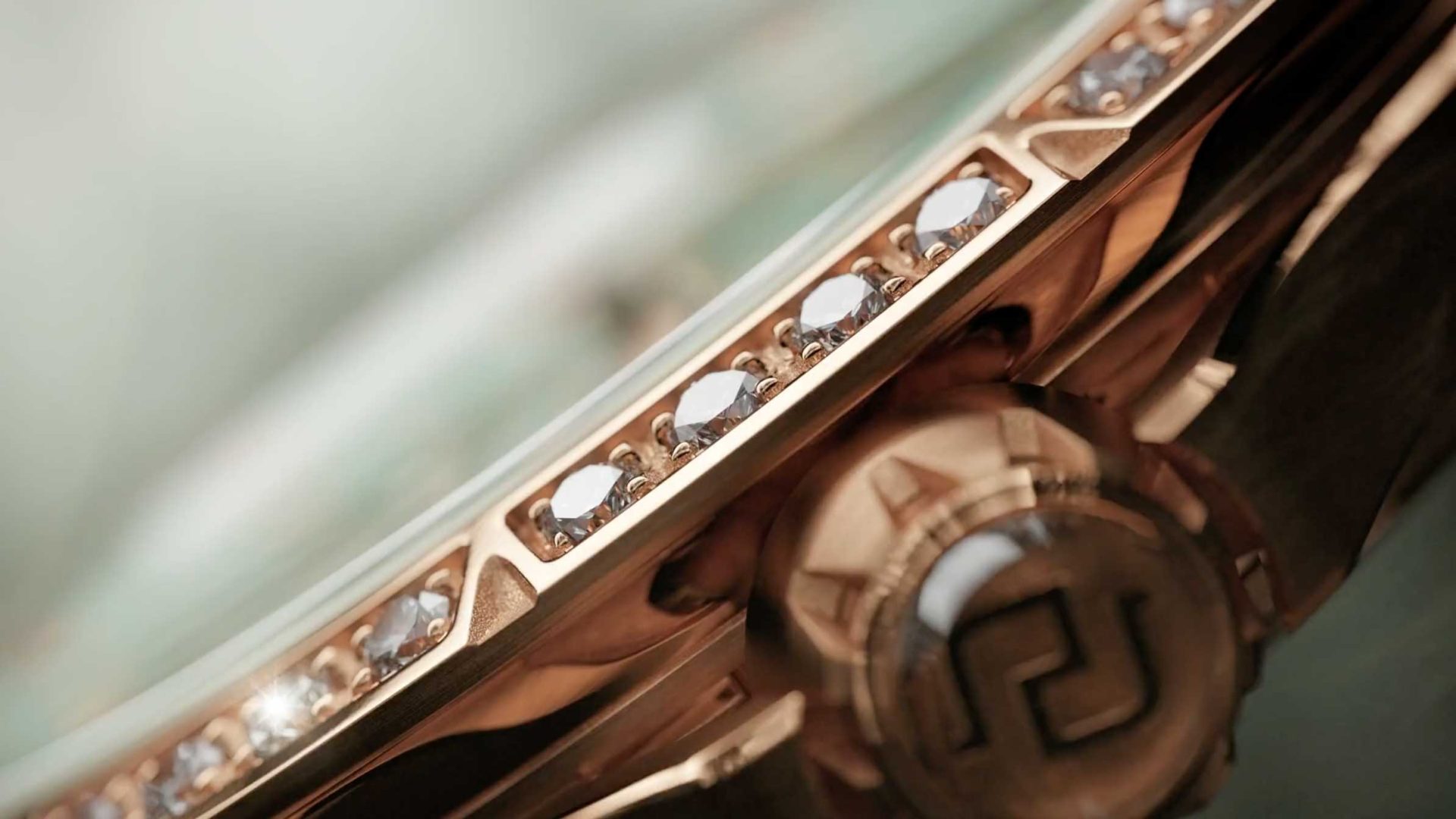 Close-up of a Roger Dubuis luxury watch bezel adorned with small diamonds and a gold crown featuring an engraved logo, showcasing fine craftsmanship and detailing. Frame from Stash Magazine article.