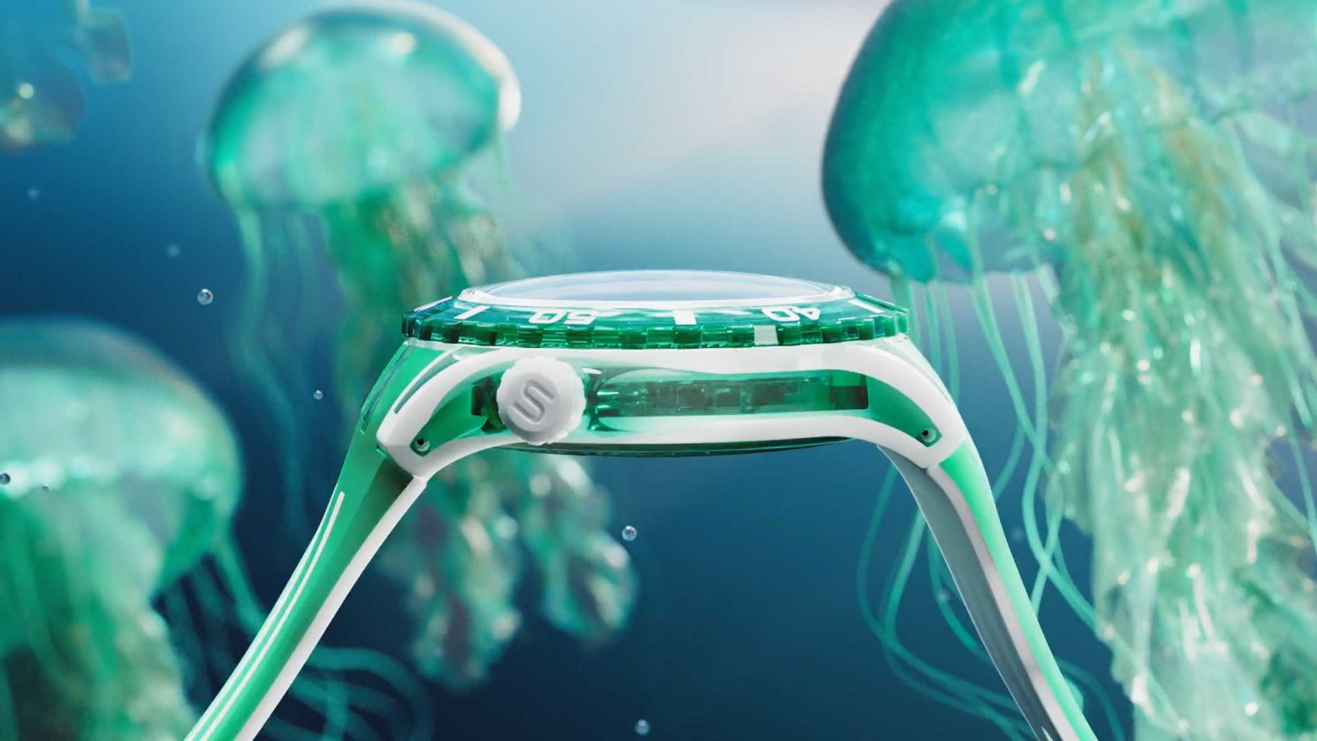A close-up side view of a green and white Swatch wristwatch underwater, surrounded by floating jellyfish in a blue ocean background. Frame from Stash Magazine article.