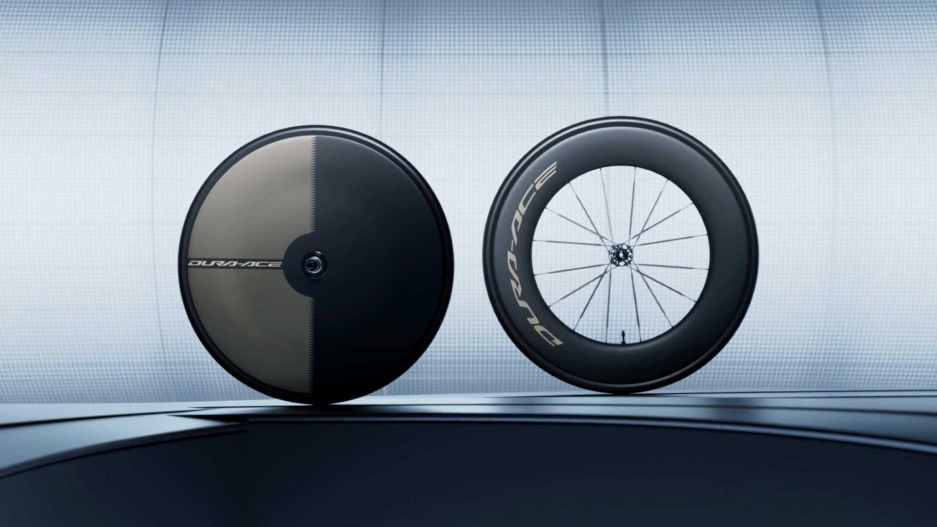 Two high-performance bicycle wheels are displayed upright. One wheel is a solid disc, while the other has spokes and a deep carbon rim. Both are labeled DURA-ACE in bold lettering on a sleek, modern background, capturing the cutting-edge innovation showcased in the Shimano DURA-ACE Campaign Film by Frame48. Frame from Stash Magazine article.