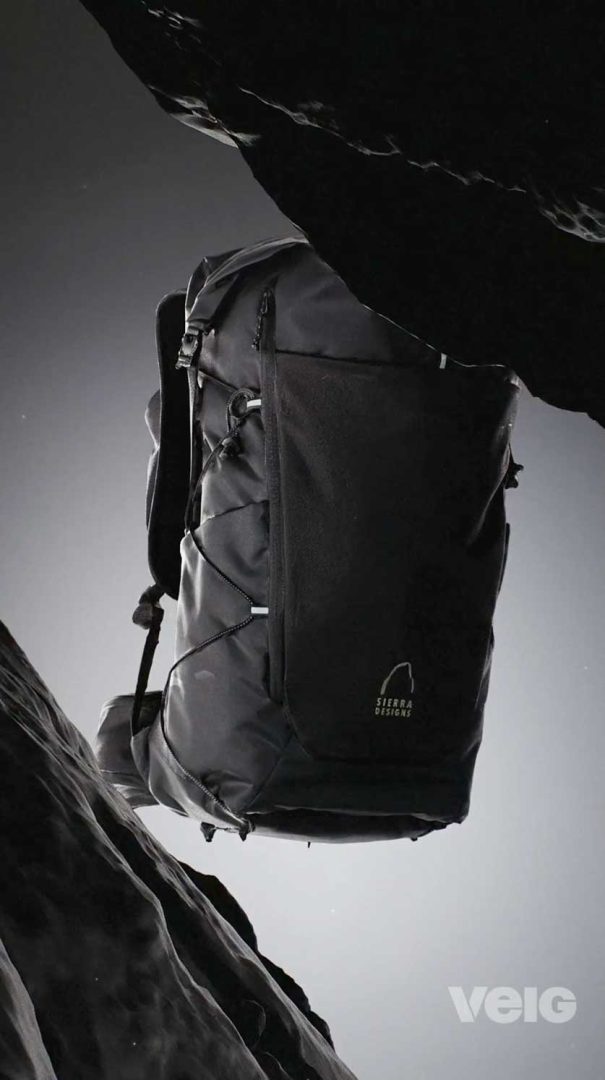 A black Sierra Designs TENAYA PACK 45L backpack is suspended in mid-air between dark, rocky surfaces, with a soft gradient background and the Velo logo in the bottom right corner. Frame from Stash Magazine article.