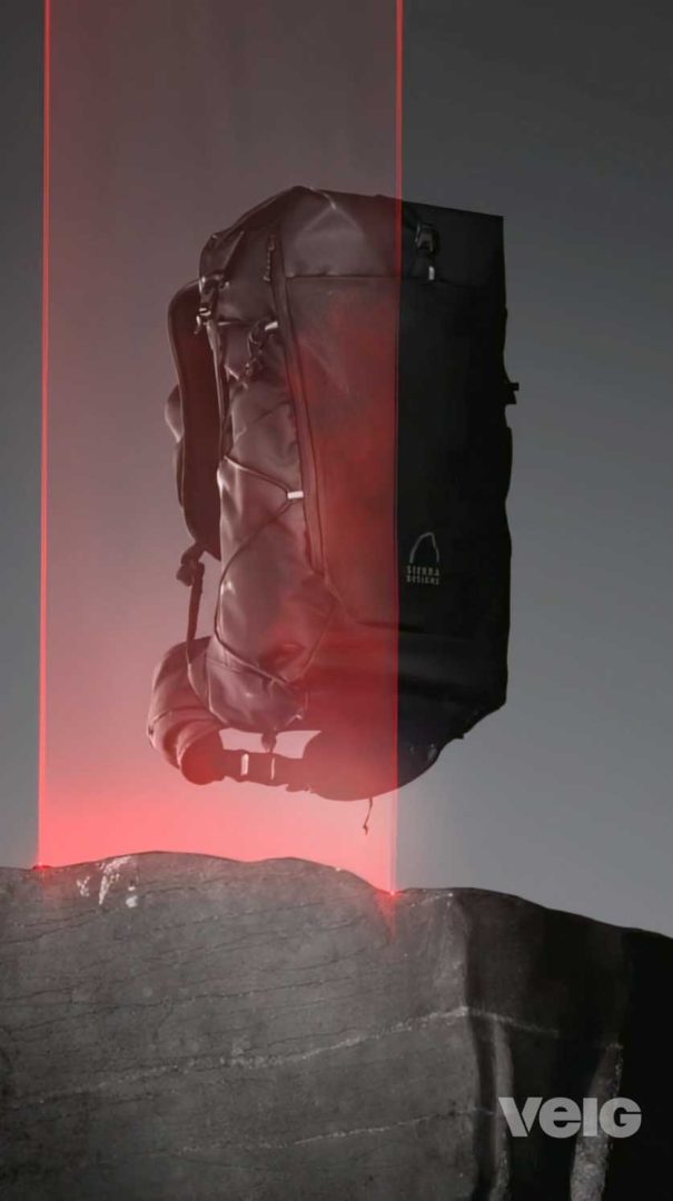 A black TENAYA PACK 45L backpack is suspended above a rocky surface, illuminated by red laser beams shining upward. The VELO logo is visible in the lower right corner. Frame from Stash Magazine article.