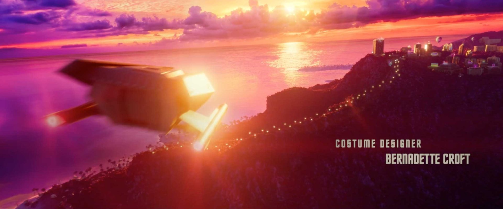 A futuristic spaceship flies over a vibrant coastal city at sunset, evoking the adventurous spirit of Star Trek: Strange New Worlds Season 4, with the credit Costume Designer: Bernadette Croft displayed on the right side. Frame from Stash Magazine article.