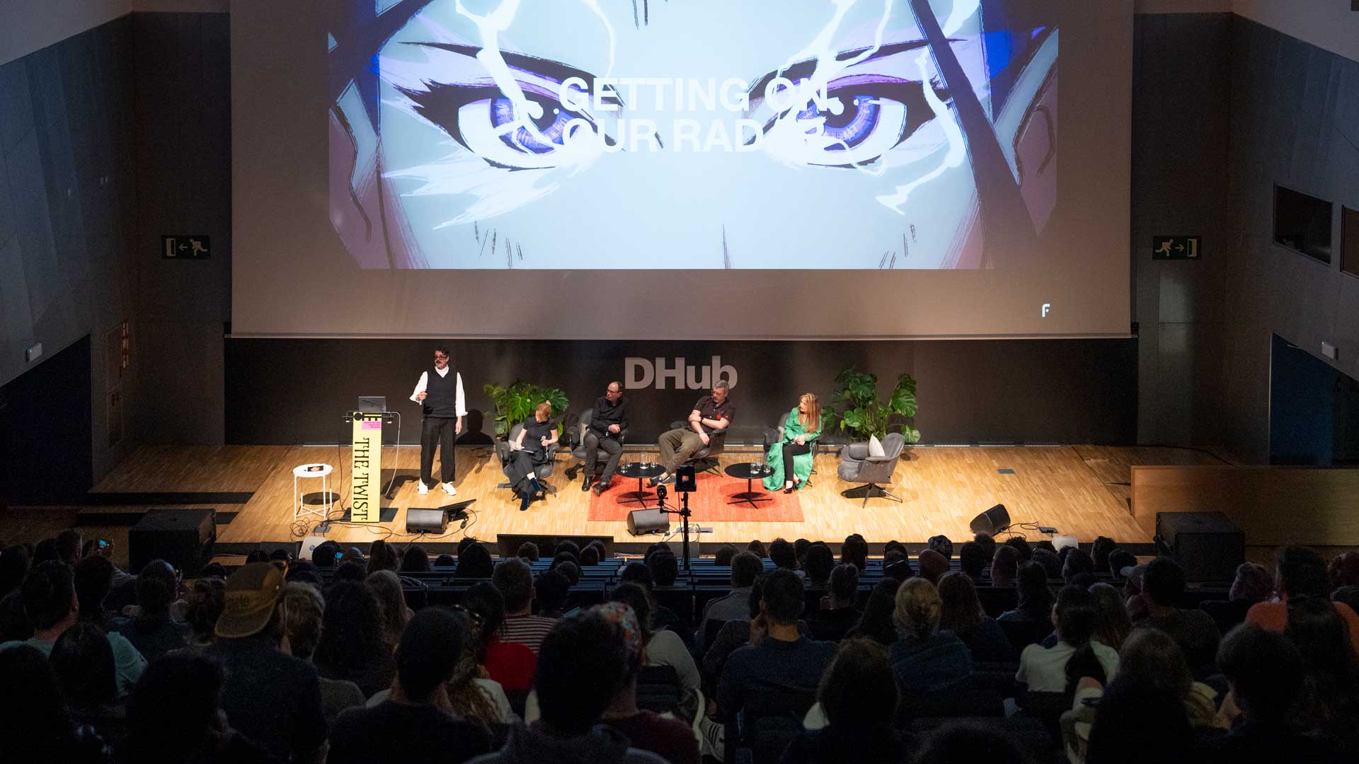 A panel of five sits onstage at a DHub conference, discussing pitching techniques in front of an audience. Behind them, a large screen displays stylized eyes and the text GETTING ON YOUR RADAR. Frame from Stash Magazine article.