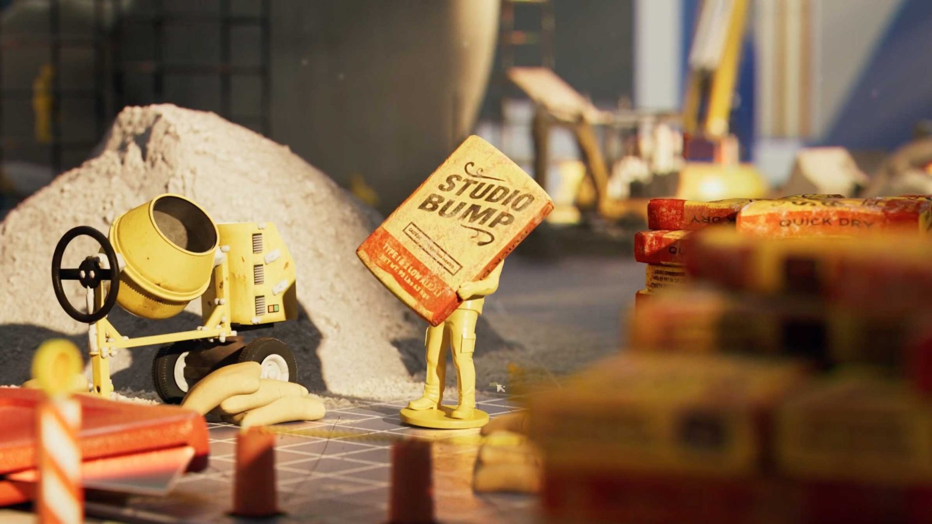 A small yellow figurine lifts a large cement bag labeled Studio Bump at a miniature construction site, complete with a cement mixer, sand pile, orange safety cones, and an "Under Construction" vibe in the background. Frame from Stash Magazine article.