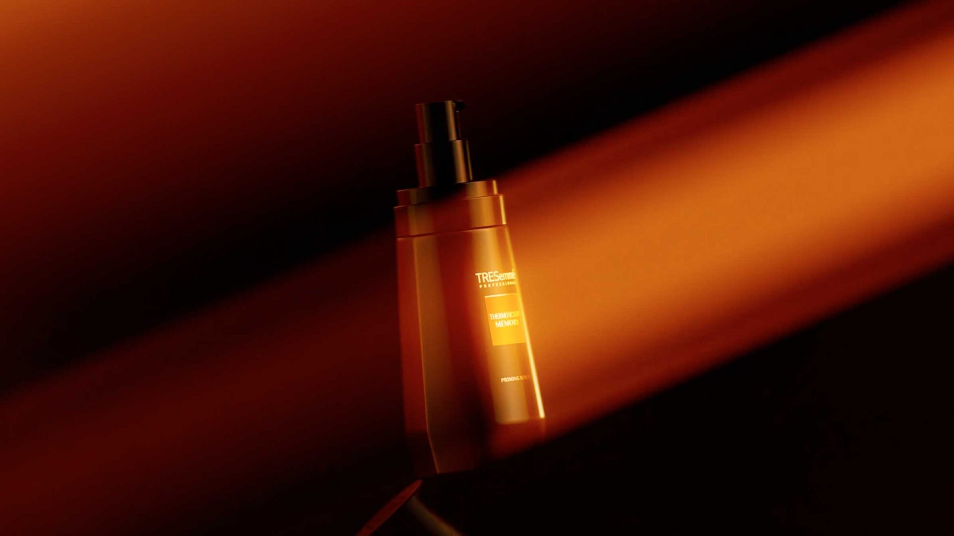 A bottle of TRESemmé Professional hair product is illuminated by a beam of orange light against a dark, blurred background, highlighting its Sculpts Memory formula in the sophisticated ambiance of Reframe Studio. Frame from Stash Magazine article.