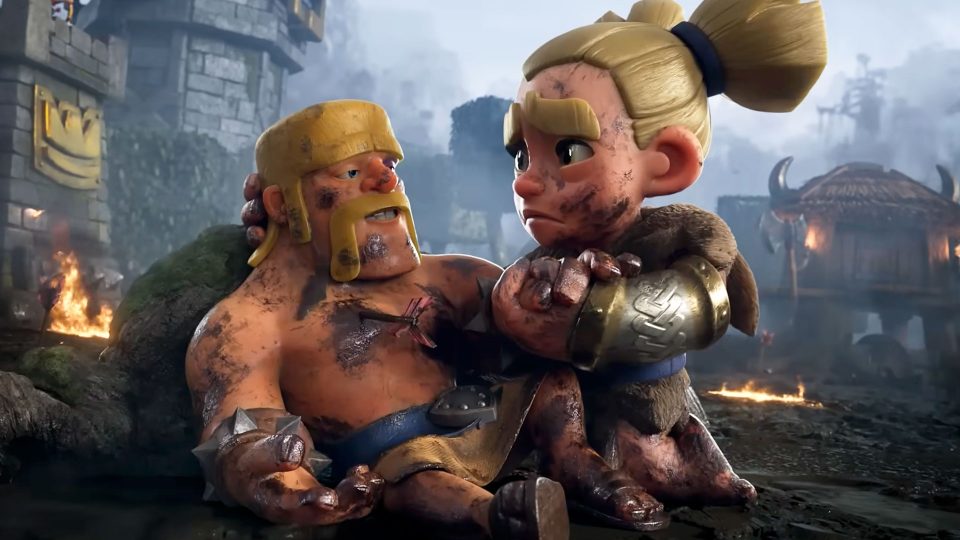 A dirty, injured cartoon warrior is comforted by a worried female fighter in armor. They sit on the ground amid a smoky, battle-damaged landscape with burning debris in the background, reminiscent of an intense Clash Royale scene. Frame from Stash Magazine article.