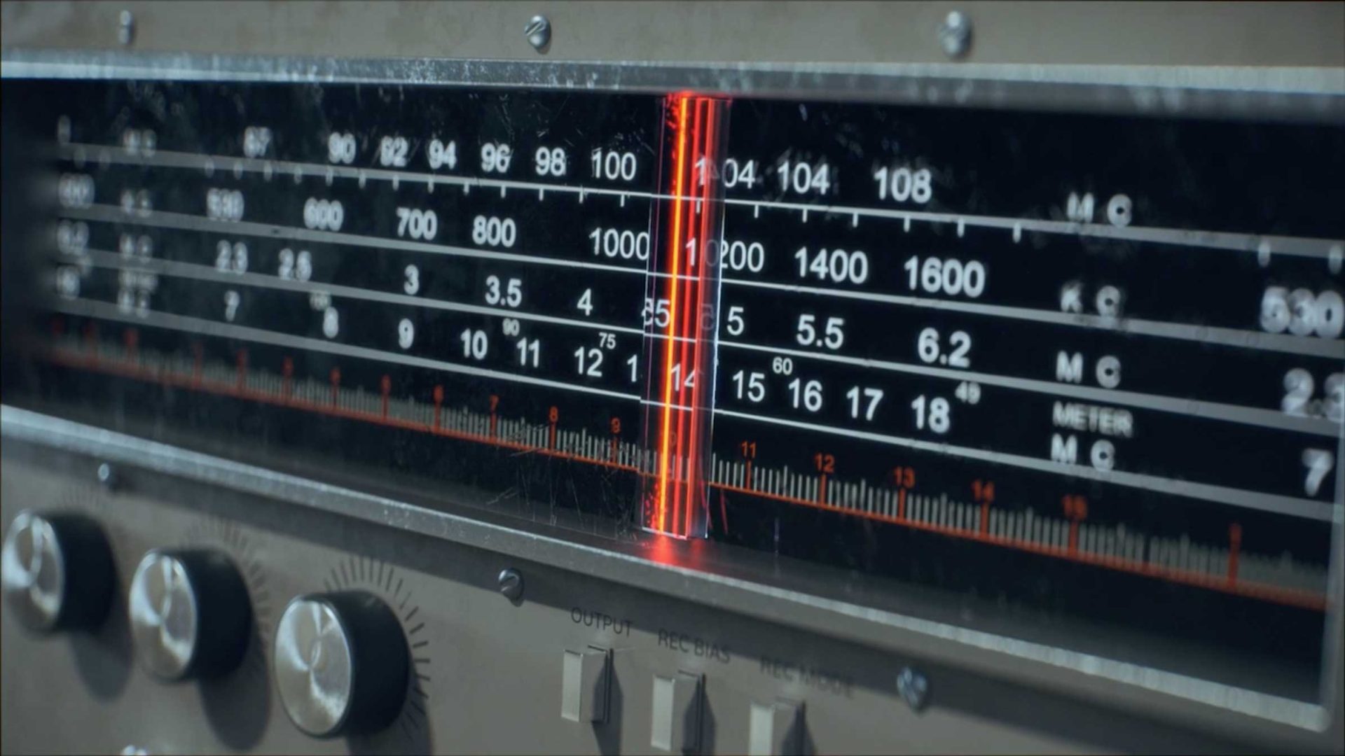 Close-up of an old-fashioned radio tuner with a red indicator light, highlighting the beauty in the details of vintage electronic devices—frequency numbers and control knobs just below the display. Frame from Stash Magazine article.