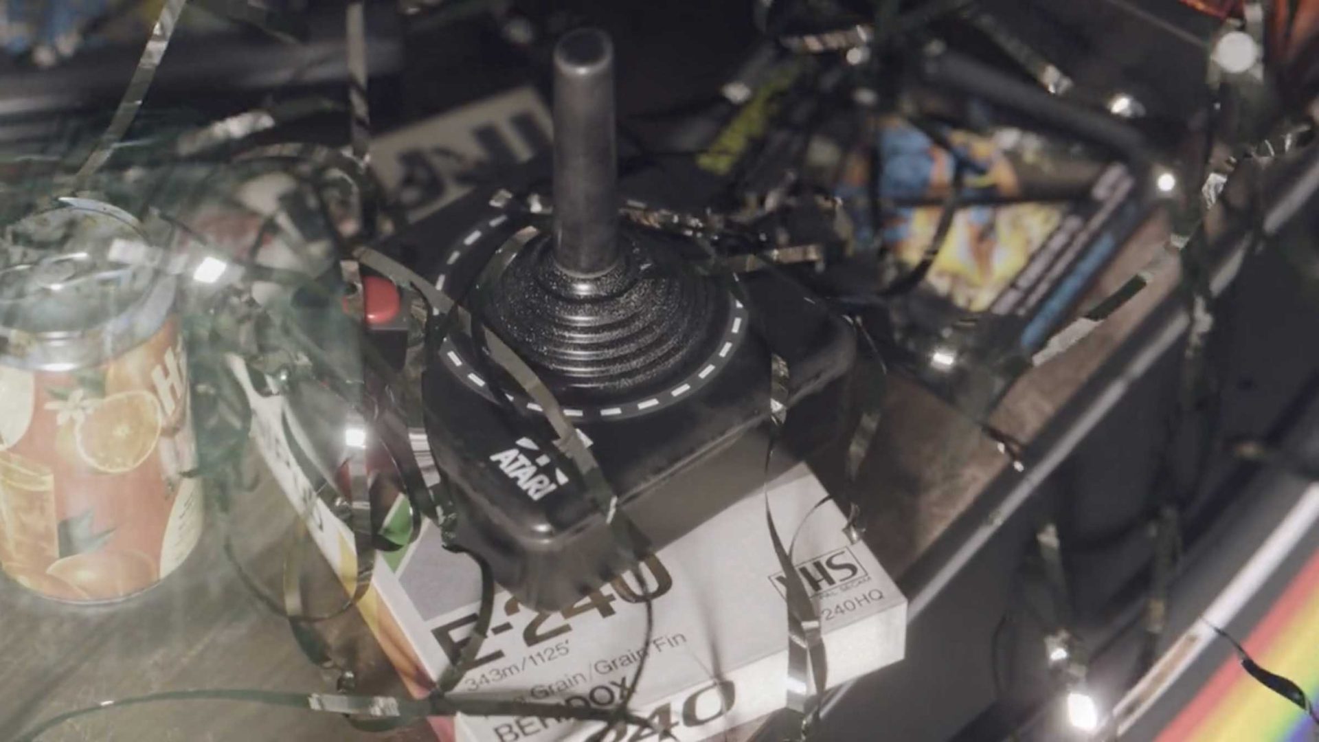 An Atari joystick sits among scattered party streamers, a soda can, and various retro items, evoking nostalgia in a cluttered scene inspired by the short film Vintage Electronic Devices by Studio Aiko. Frame from Stash Magazine article.