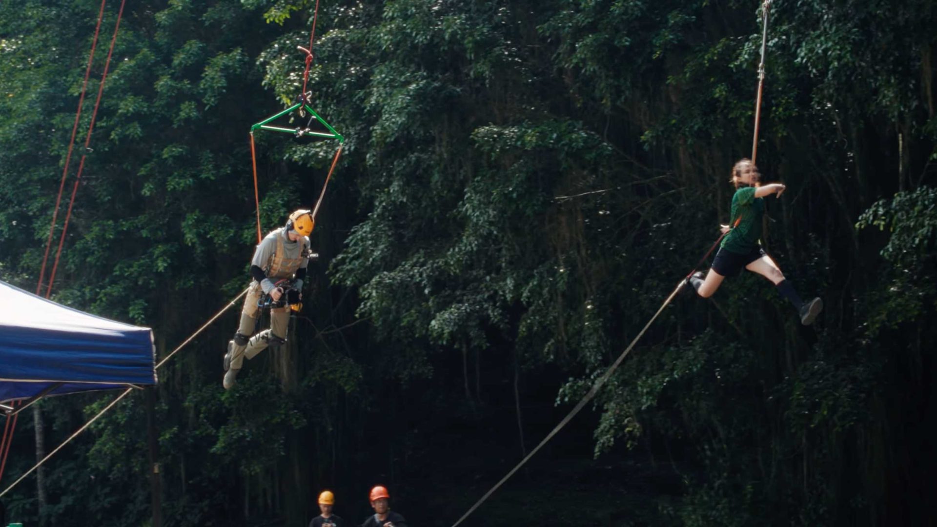 Two people secured with harnesses and ropes are suspended in midair near a lush rainforest canopy. Crew members in helmets stand below, monitoring the activity—a scene brought to life by Studio Birthplace for WWF. Frame from Stash Magazine article.